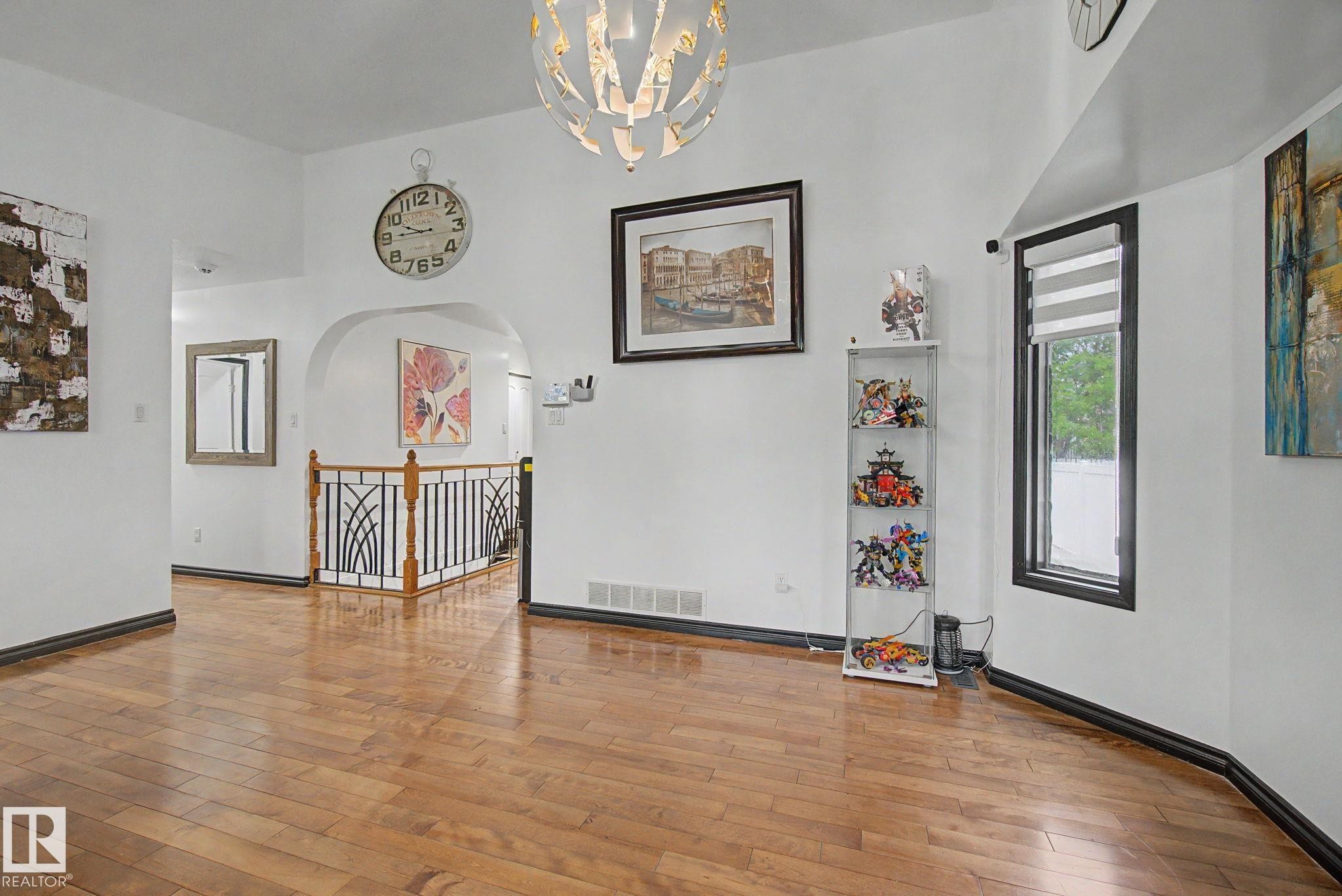 Hardwood-finish flooring extends throughout this expansive area, featuring an arched doorway, black baseboards, and a contemporary chandelier - 242 Northmount Drive, Wetaskiwin, AB