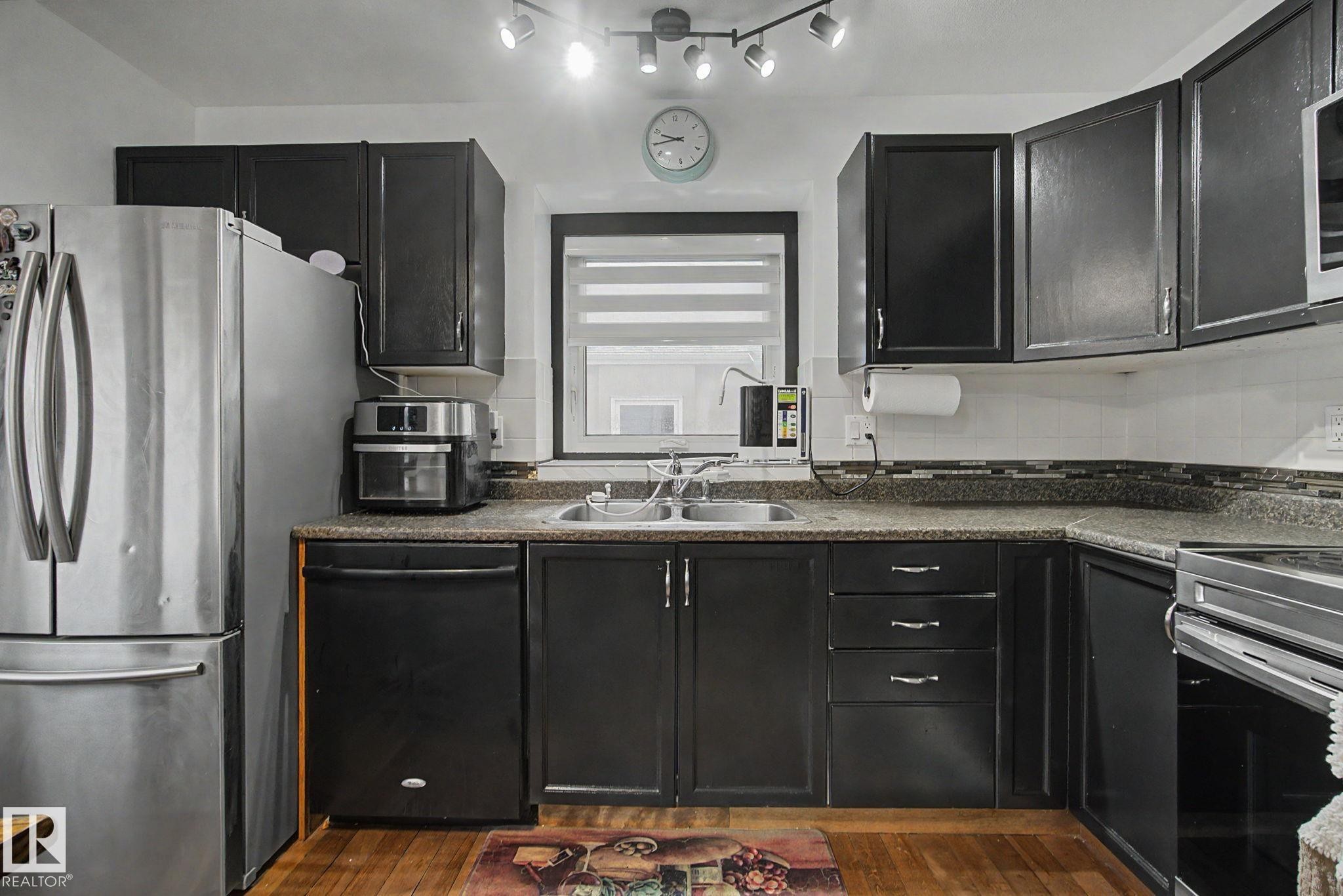 Kitchen featuring dark cabinetry, light-colored countertops, stainless steel refrigerator, and wood-finish flooring - 242 Northmount Drive, Wetaskiwin, AB