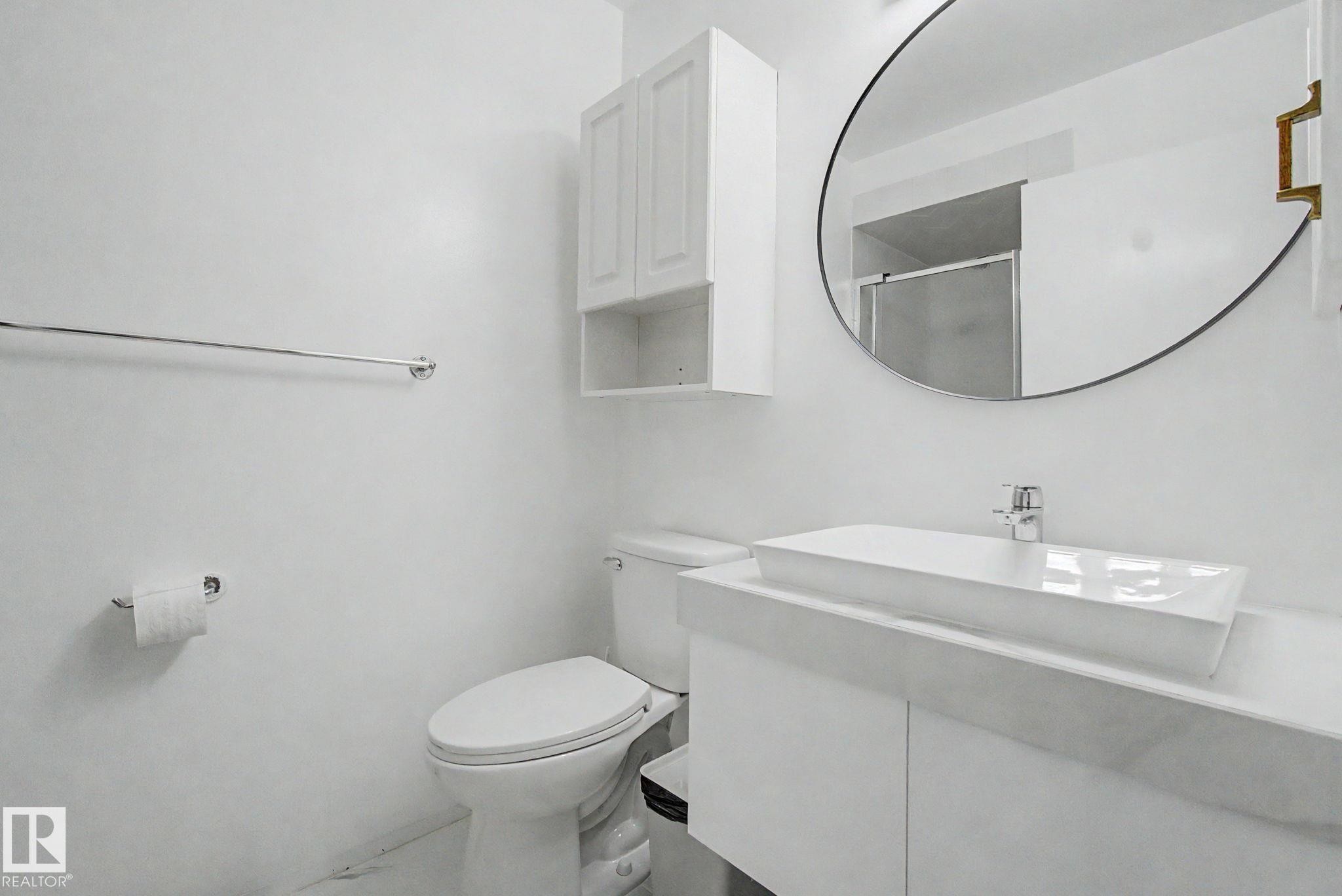 Contemporary bathroom featuring a rectangular vessel sink, white vanity, round wall mirror, wall-mounted cabinetry, and chrome fixtures - 242 Northmount Drive, Wetaskiwin, AB