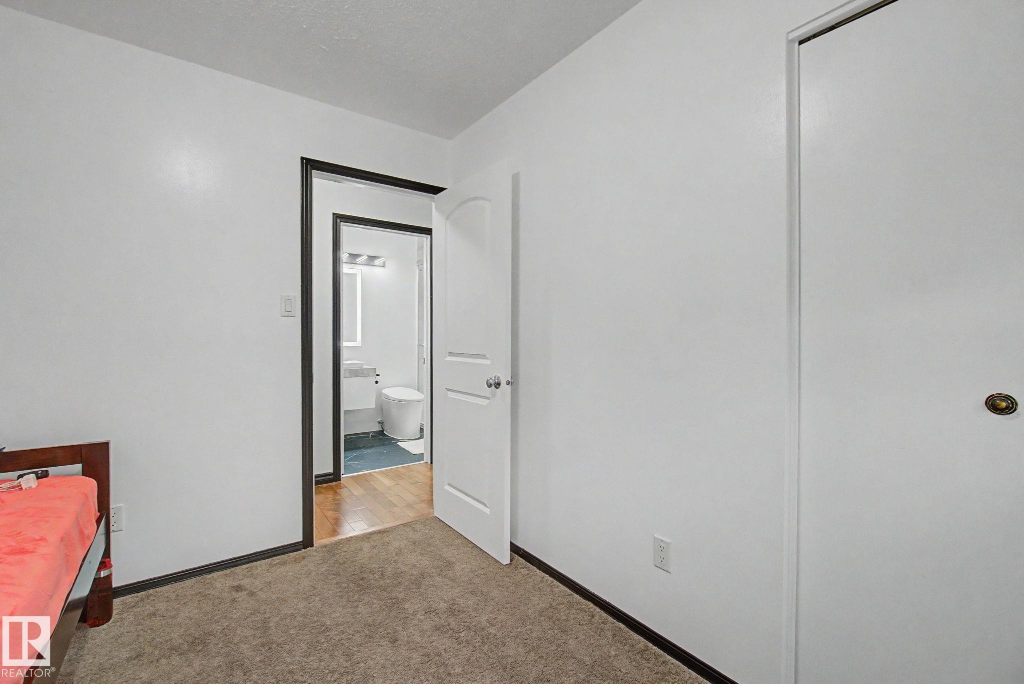 Carpeted room with white walls and dark trim, featuring a white door and a closet with a brass-toned knob - 242 Northmount Drive, Wetaskiwin, AB