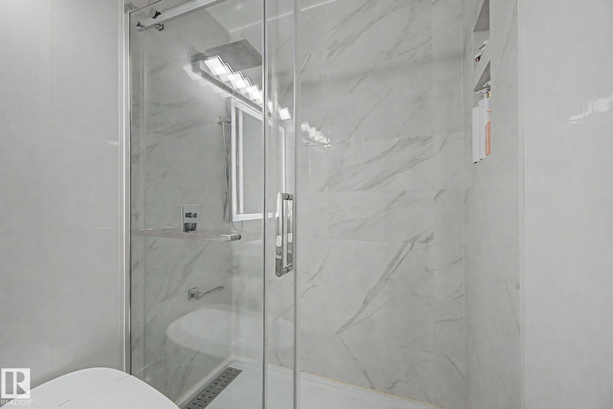 Glass-enclosed shower featuring large format tile walls with subtle veining, a built-in shower niche, a linear drain, and brushed nickel fixtures - 242 Northmount Drive, Wetaskiwin, AB