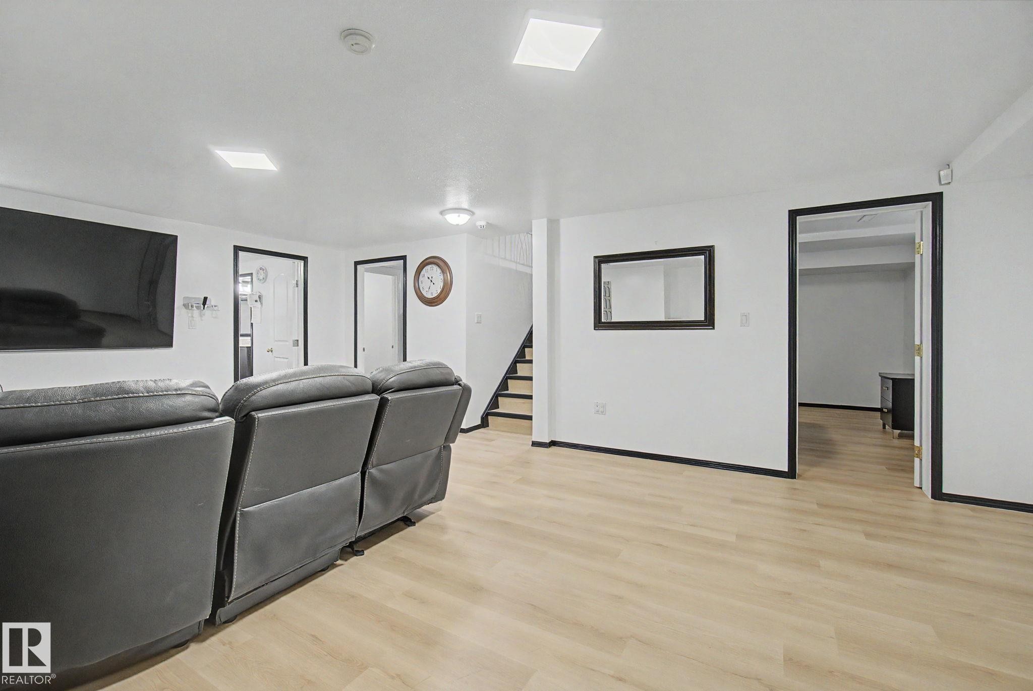 Spacious entertainment area featuring light wood-finish flooring, white walls, and contrasting black trim - 242 Northmount Drive, Wetaskiwin, AB