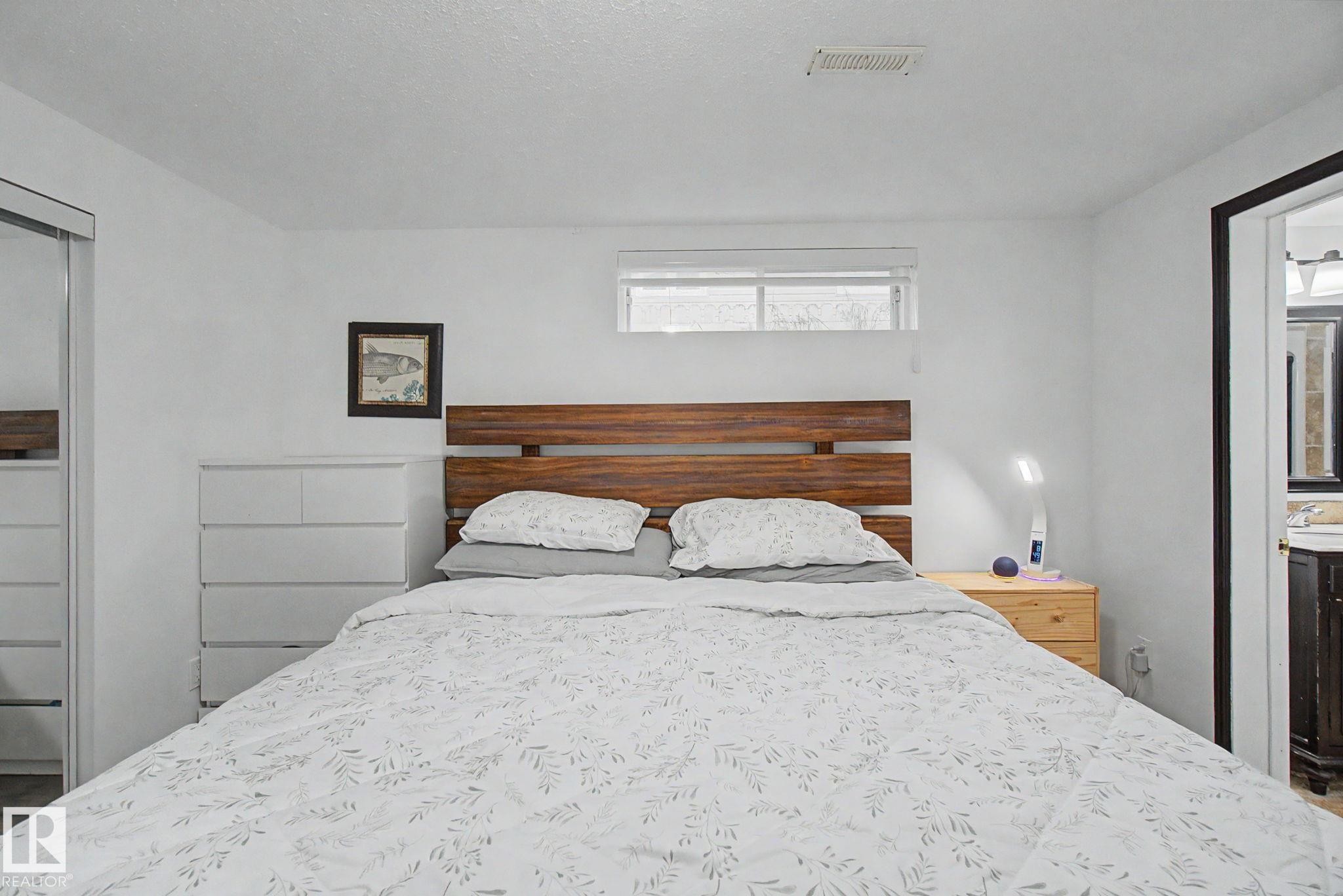Spacious sleeping area featuring a wood-finish headboard, a window with a white blind, and a white ceiling - 242 Northmount Drive, Wetaskiwin, AB