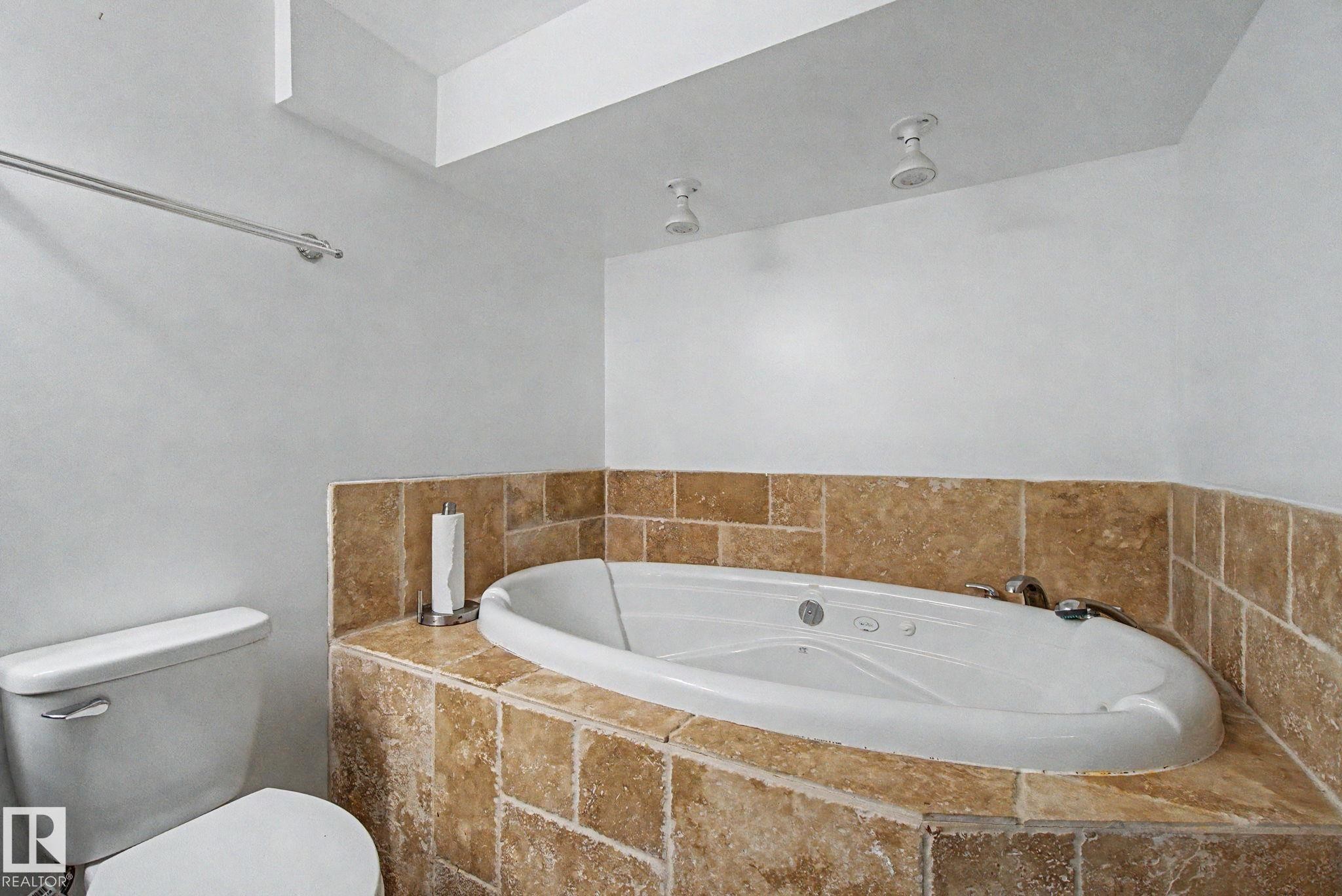Built-in soaking tub with a tiled surround, recessed ceiling lighting, and a chrome towel bar - 242 Northmount Drive, Wetaskiwin, AB