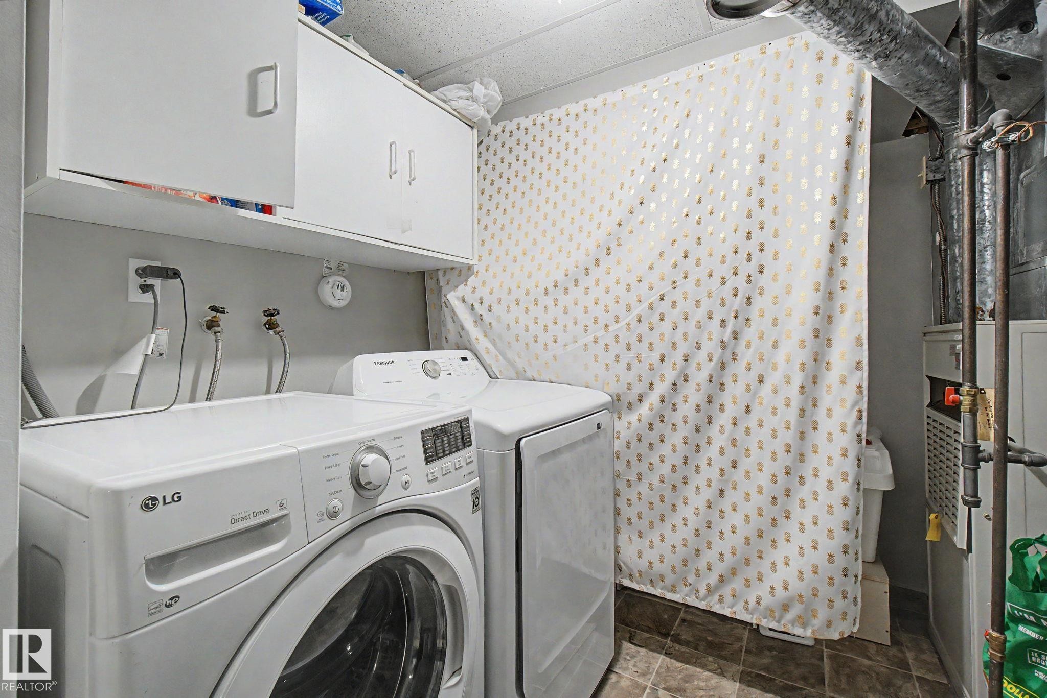 Dedicated laundry area featuring white upper cabinetry, tiled flooring, and exposed utility piping - 242 Northmount Drive, Wetaskiwin, AB