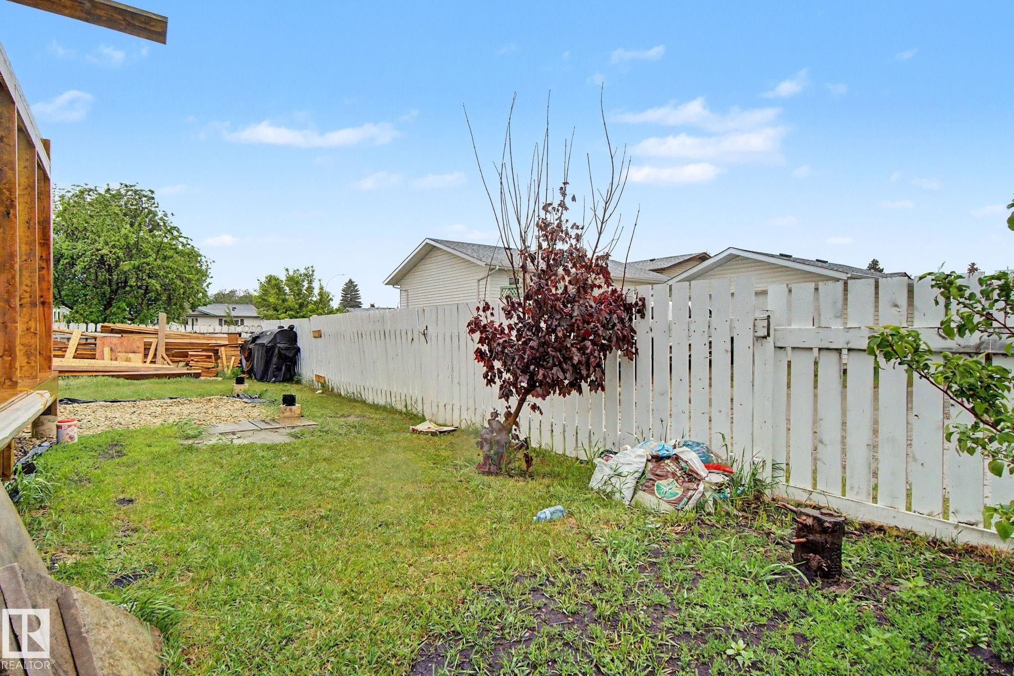 Grassed backyard featuring a white picket fence and mature landscaping - 242 Northmount Drive, Wetaskiwin, AB