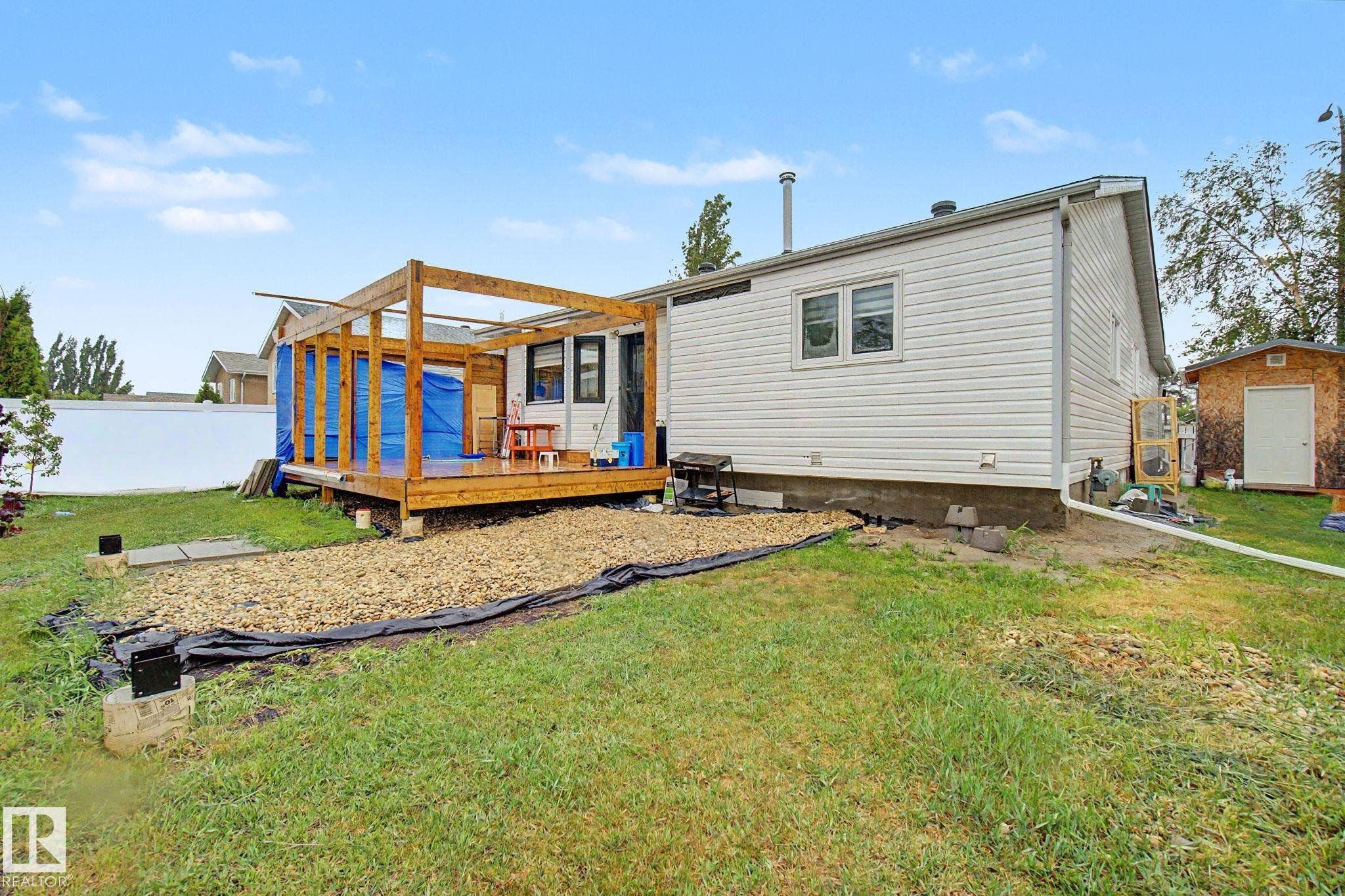 Rear exterior featuring a wood deck with an open pergola frame, white vinyl siding, a gravel area, a small shed, and a privacy fence - 242 Northmount Drive, Wetaskiwin, AB