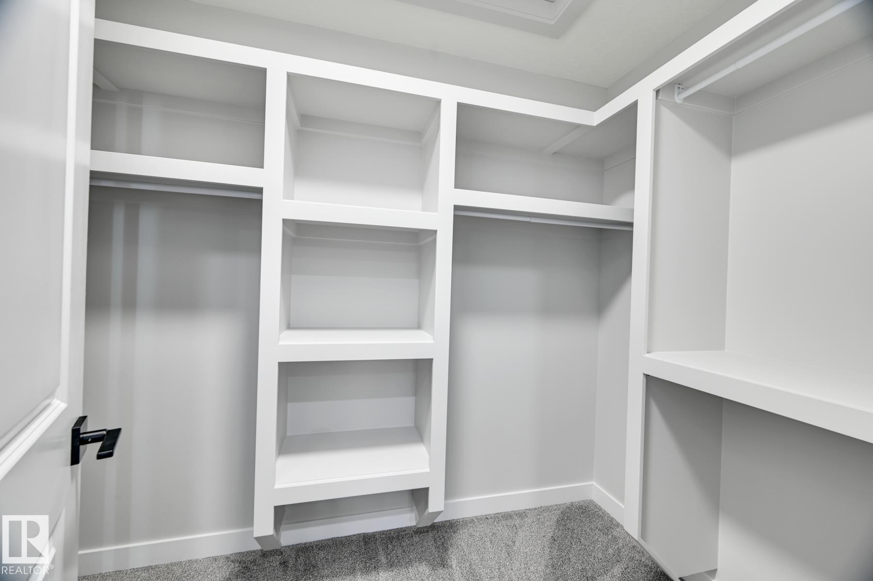 Walk-in closet featuring built-in white shelving, multiple hanging rods, and gray carpet flooring - 54 Chartres Close, St. Albert, AB - Indoor With Storage