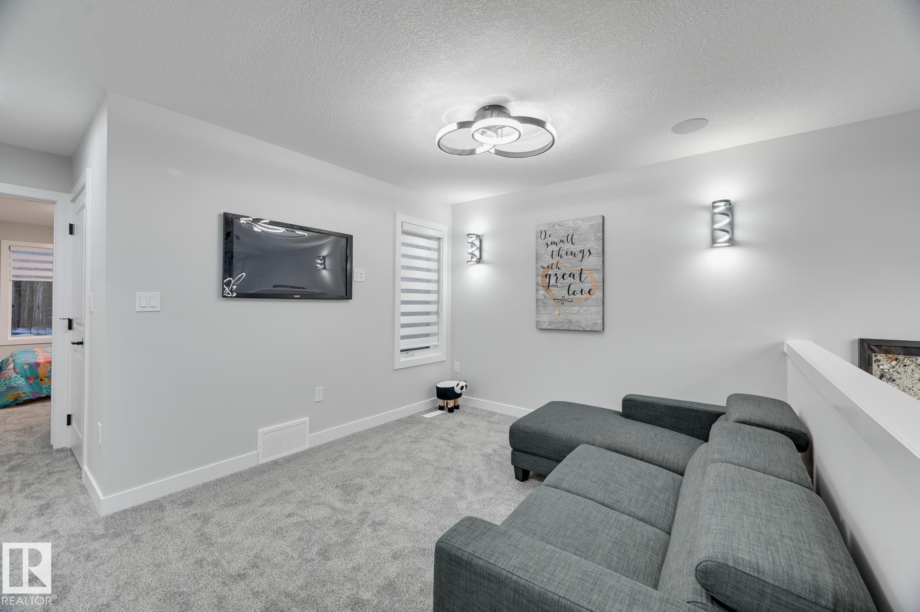 Carpeted room featuring a ceiling-mounted light fixture, wall-mounted television, and two sconce lights - 54 Chartres Close, St. Albert, AB - Indoor