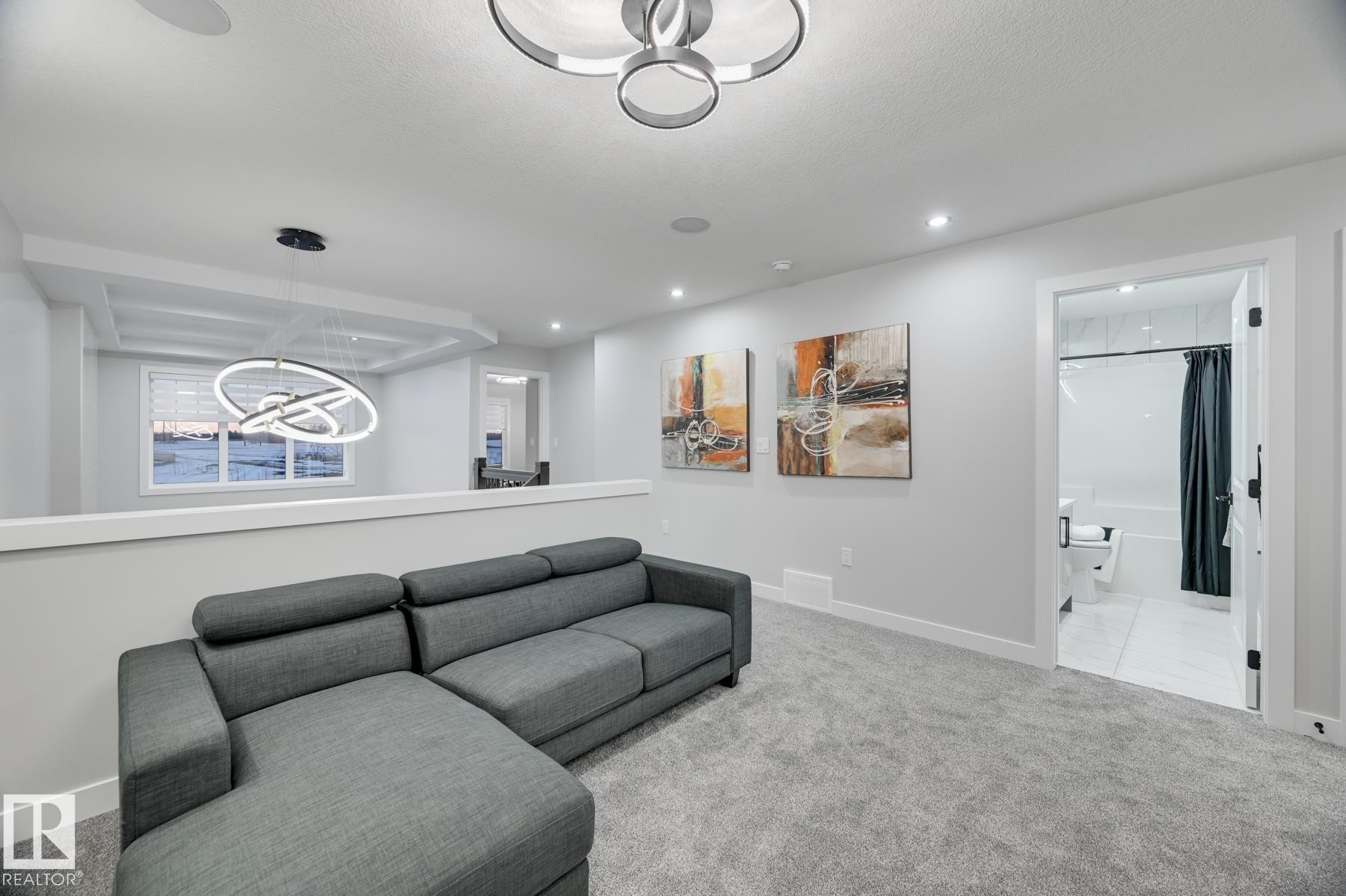 Carpeted common area featuring recessed lighting and a contemporary ceiling fixture, with a half-wall partition and an open doorway revealing a bathroom with a white tub-shower combination - 54 Chartres Close, St. Albert, AB - Indoor