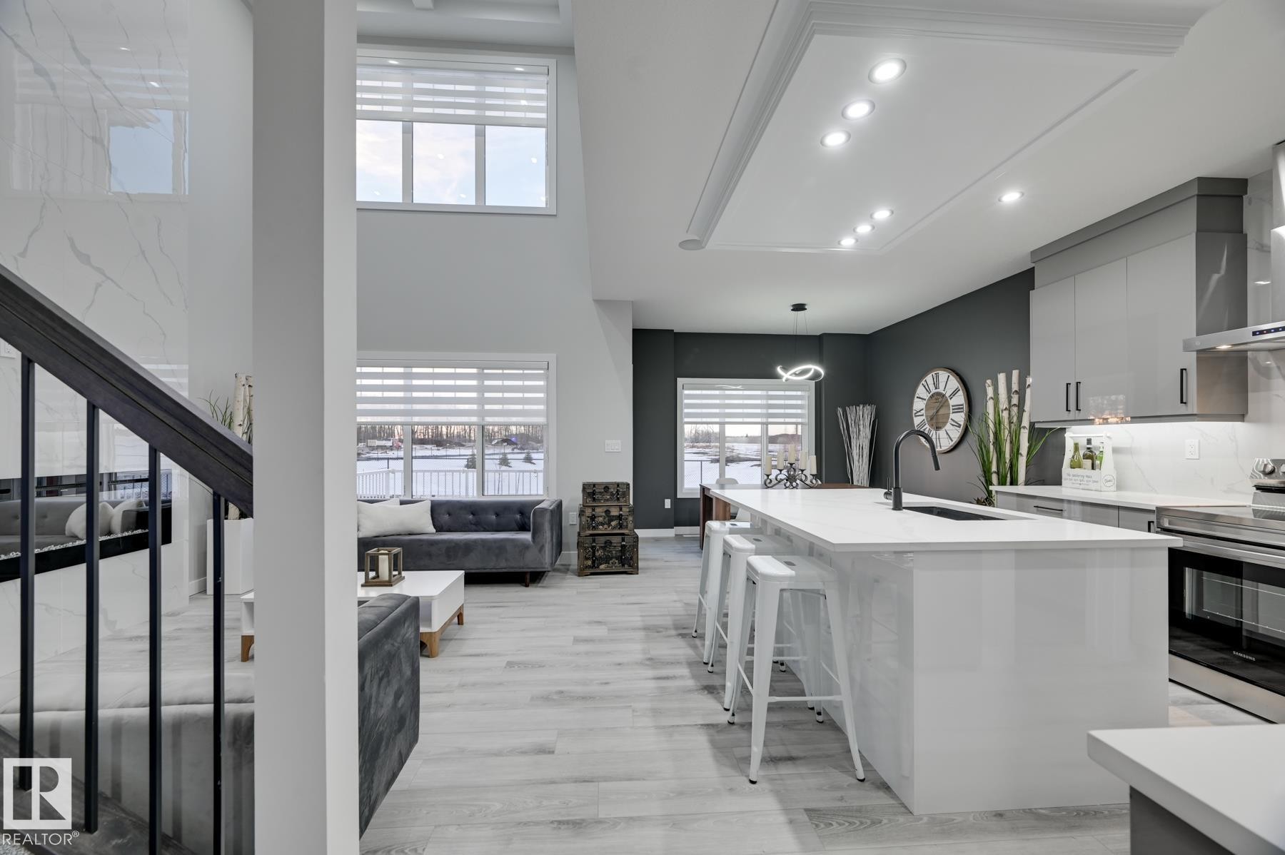 Open-concept kitchen and living area featuring high ceilings, light wood-finish flooring, a white kitchen island with a dark faucet, stainless steel appliances, and a dark accent wall - 54 Chartres Close, St. Albert, AB - Indoor Photo Showing Kitchen With Upgraded Kitchen