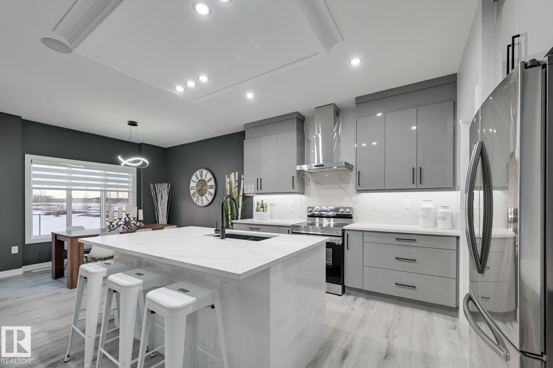Contemporary kitchen featuring an oversized island with countertop seating, glossy gray cabinetry, stainless steel appliances, and wood-finish flooring - 54 Chartres Close, St. Albert, AB - Indoor Photo Showing Kitchen With Upgraded Kitchen