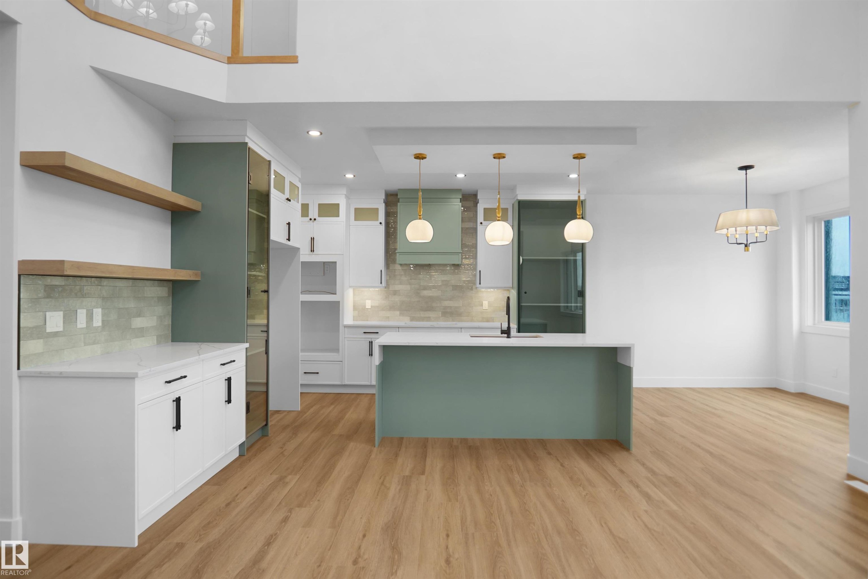 Open-concept kitchen featuring an expansive island with a light green base, three pendant lights, and wood-finish flooring - 142 Edgewater Circle, Leduc, AB