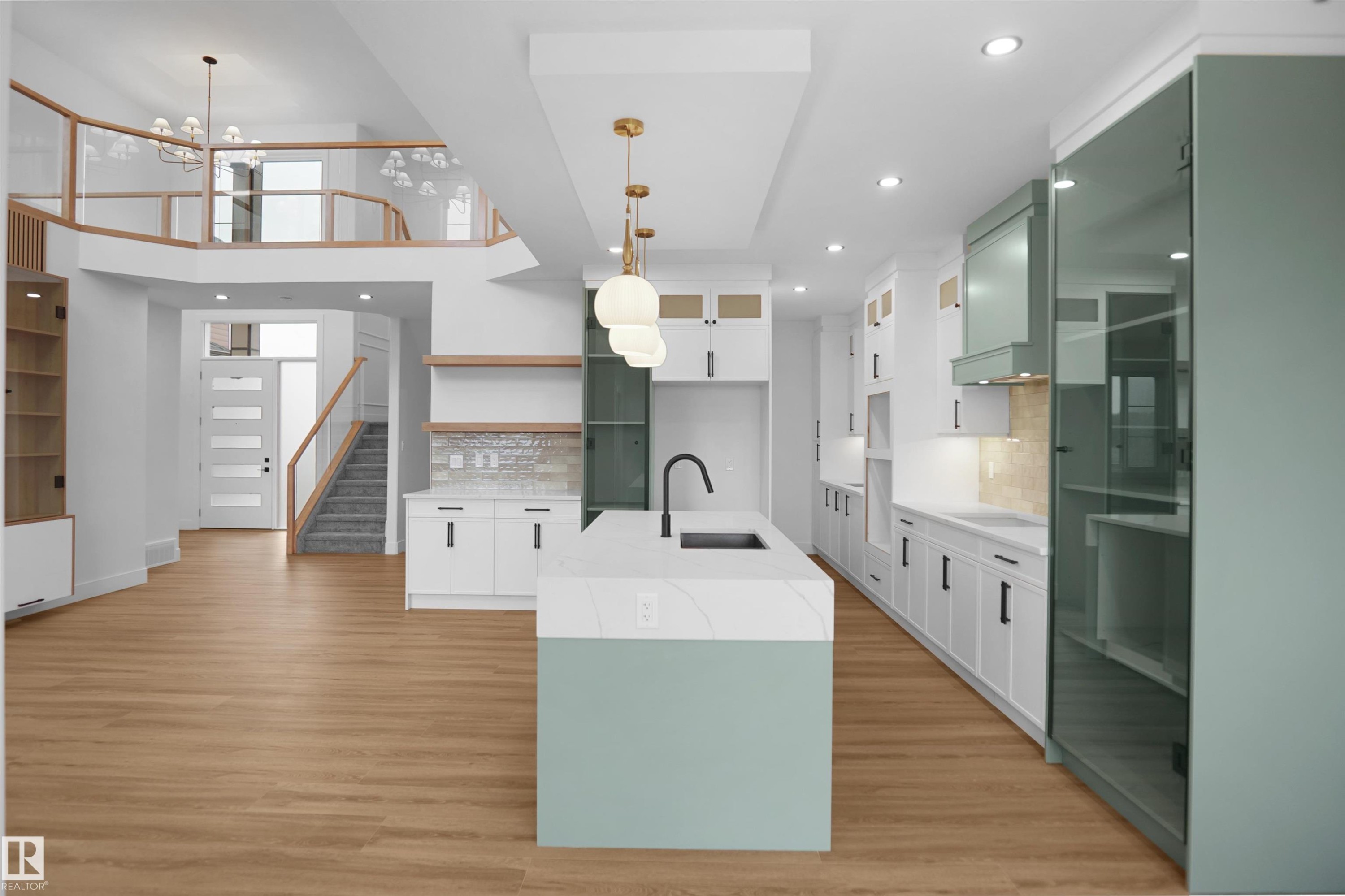 Open-concept kitchen featuring a center island with a light green base and a light-toned countertop, wood-finish flooring, white cabinetry with black hardware, recessed lighting, and a textured backsplash - 142 Edgewater Circle, Leduc, AB