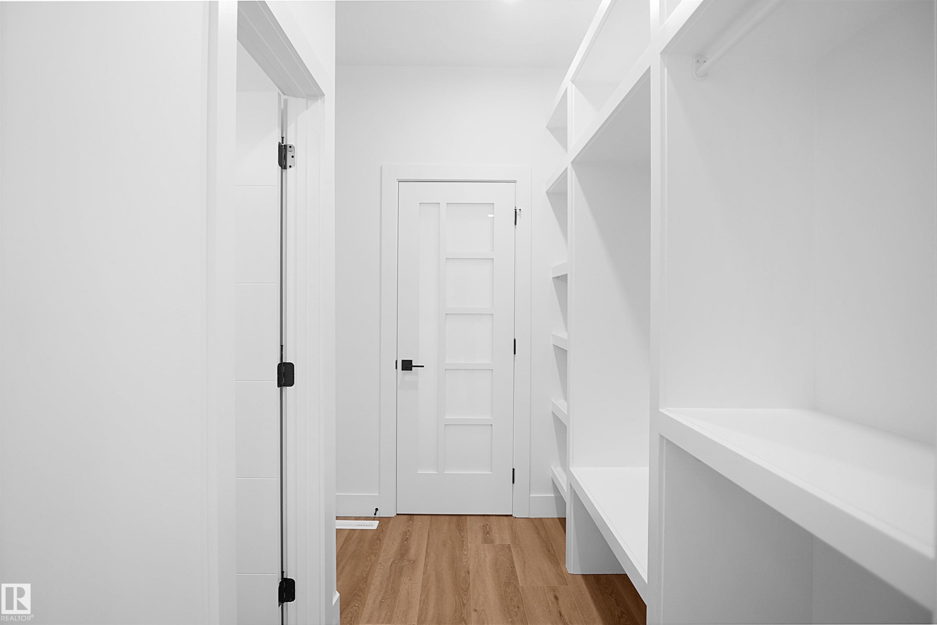 Walk-through closet with extensive built-in shelving, wood-finish flooring, white walls, and a five-lite interior door with matte black hardware - 142 Edgewater Circle, Leduc, AB