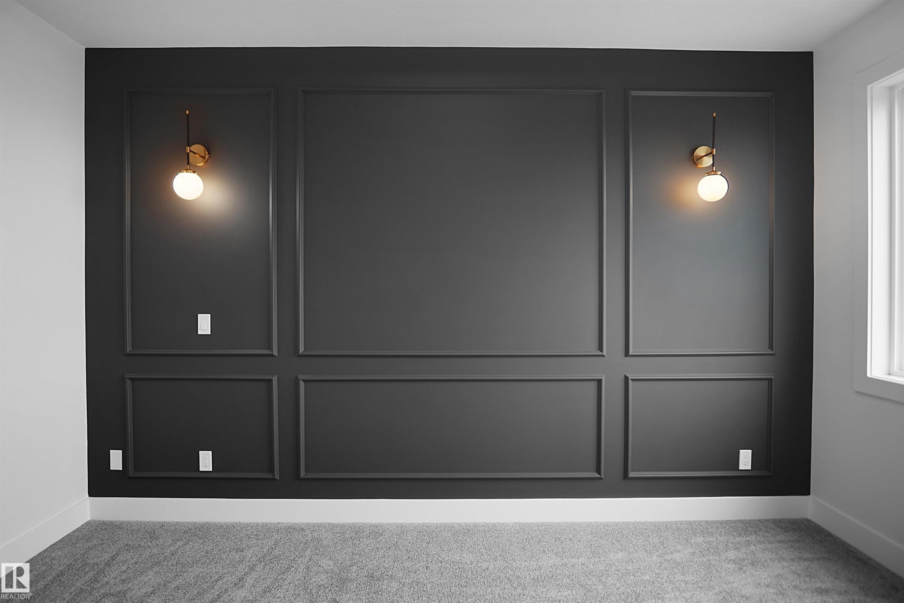 Accent wall featuring dark paneling with decorative trim, two wall-mounted sconces with spherical glass shades, and light gray carpeting - 142 Edgewater Circle, Leduc, AB