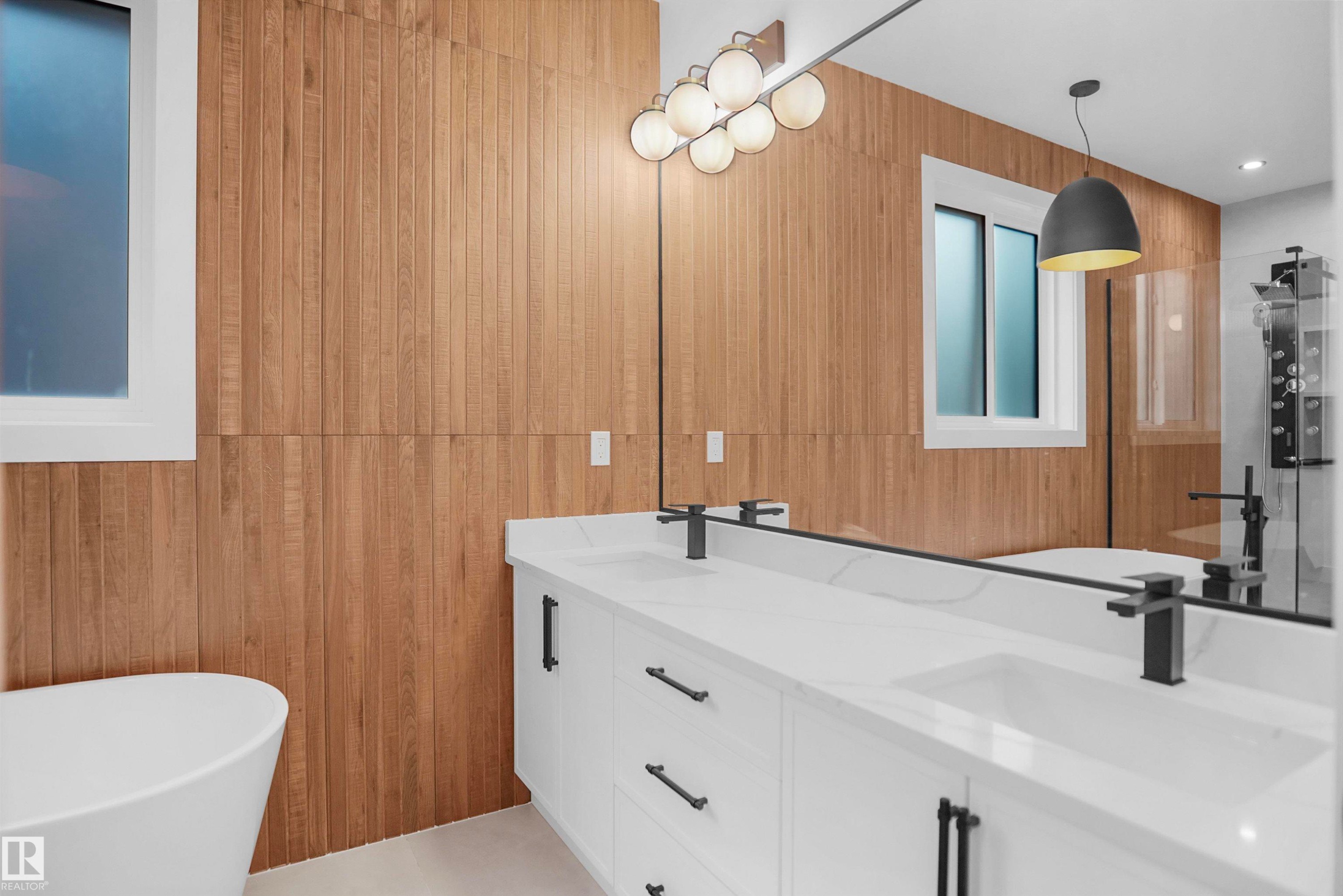 Modern bathroom featuring a double vanity with white cabinetry and integrated sinks, matte black fixtures, a white freestanding soaking tub, and vertical wood-finish wall paneling - 142 Edgewater Circle, Leduc, AB