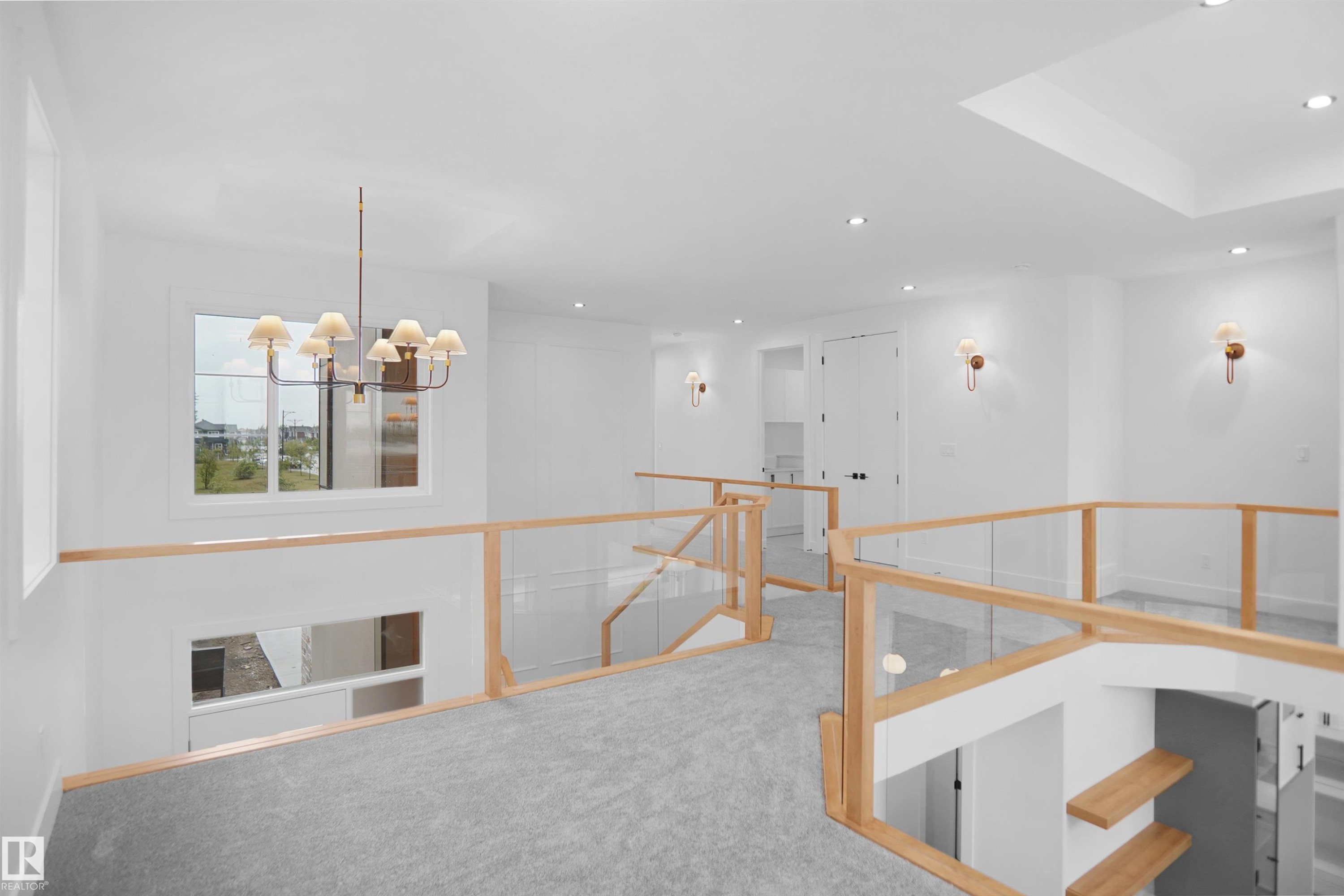 Upper-level landing featuring light gray carpeting, clear glass railings with wood-finish tops, a prominent ceiling-mounted chandelier, recessed lighting, and wall sconces - 142 Edgewater Circle, Leduc, AB