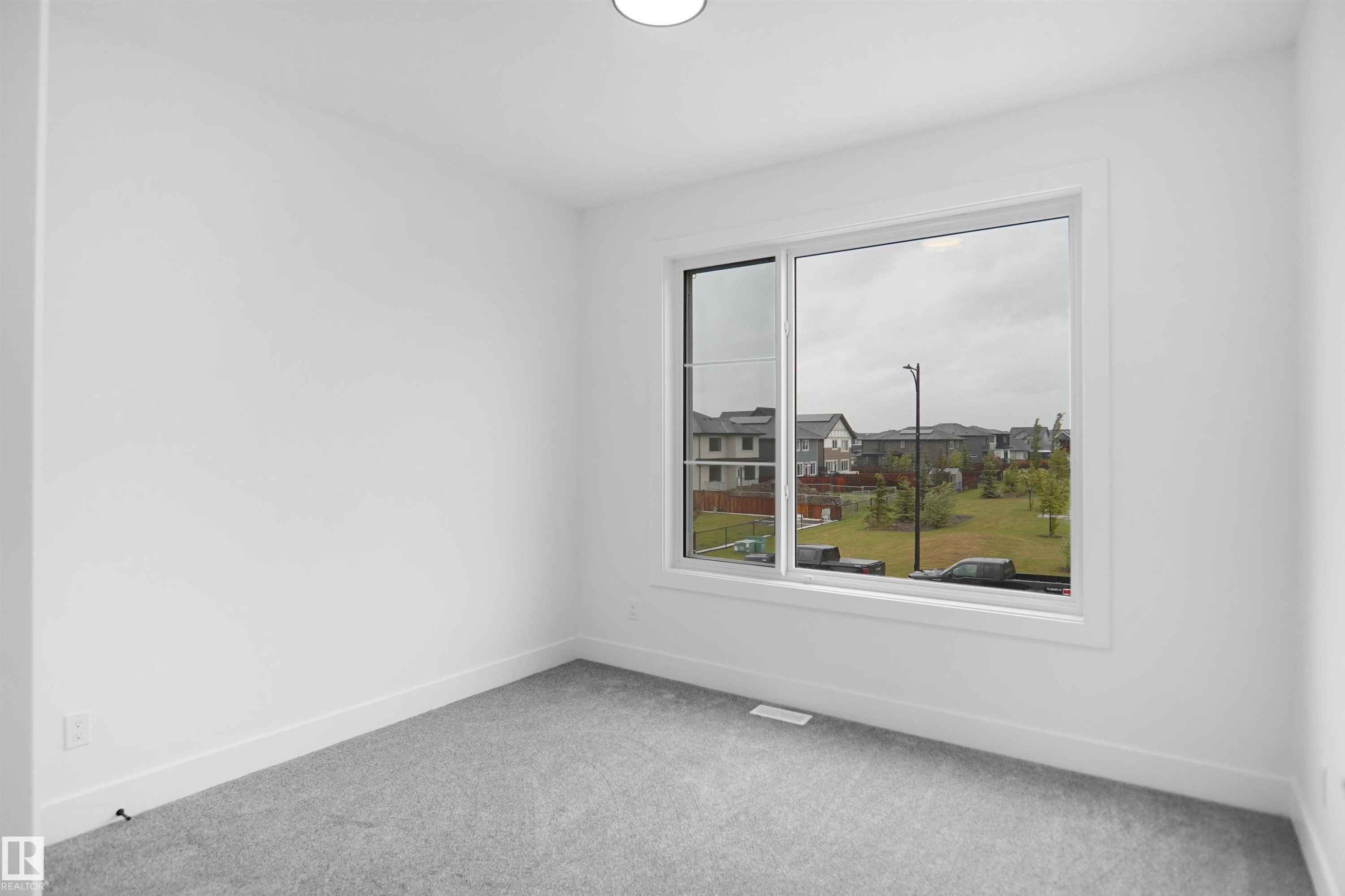 Interior room featuring a large window, light gray carpeting, white walls, white baseboards, and a ceiling-mounted light fixture - 142 Edgewater Circle, Leduc, AB