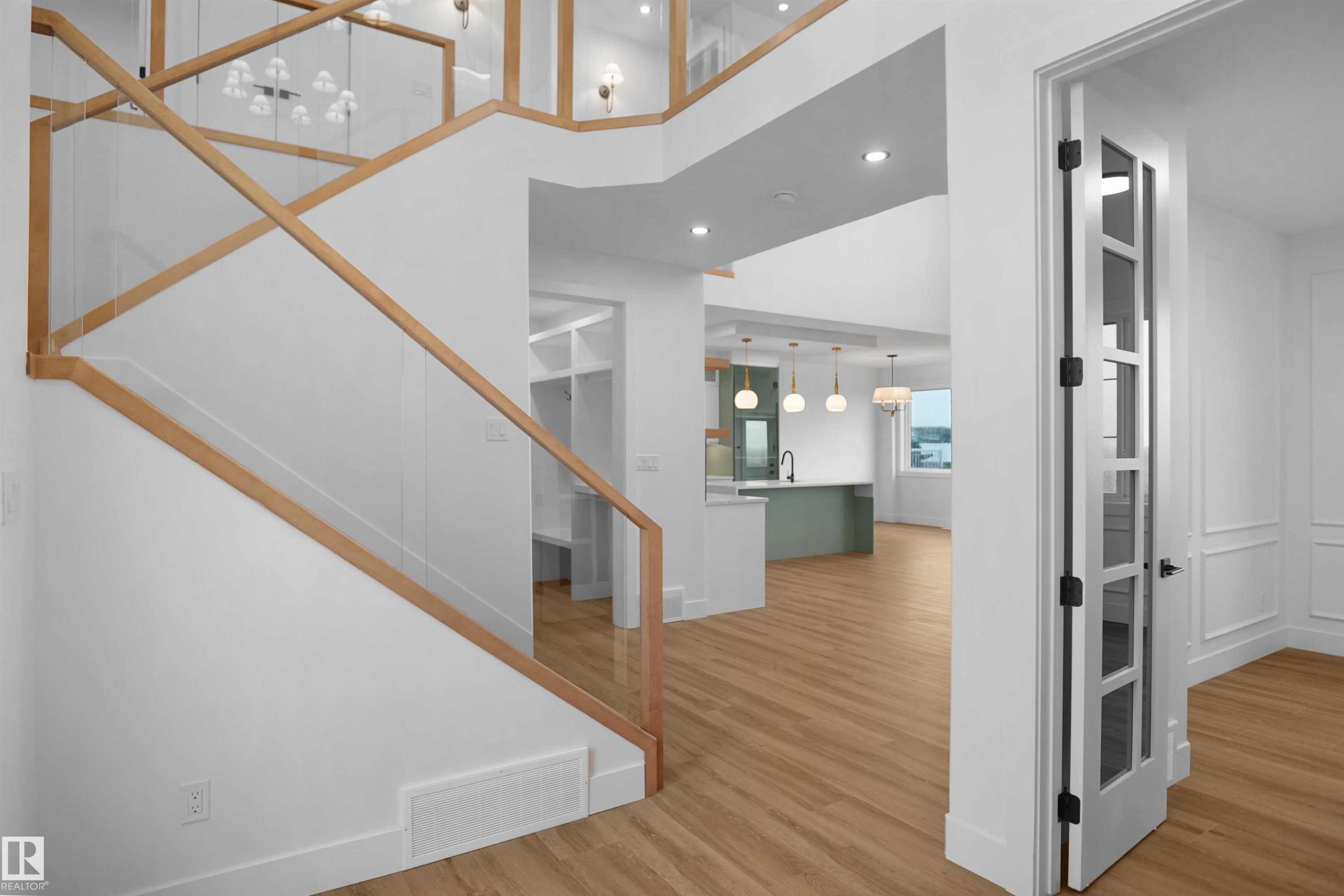 Open-concept interior featuring wood-finish flooring, a modern staircase with glass panels and wood handrails, recessed lighting, and a kitchen island with pendant lighting - 142 Edgewater Circle, Leduc, AB