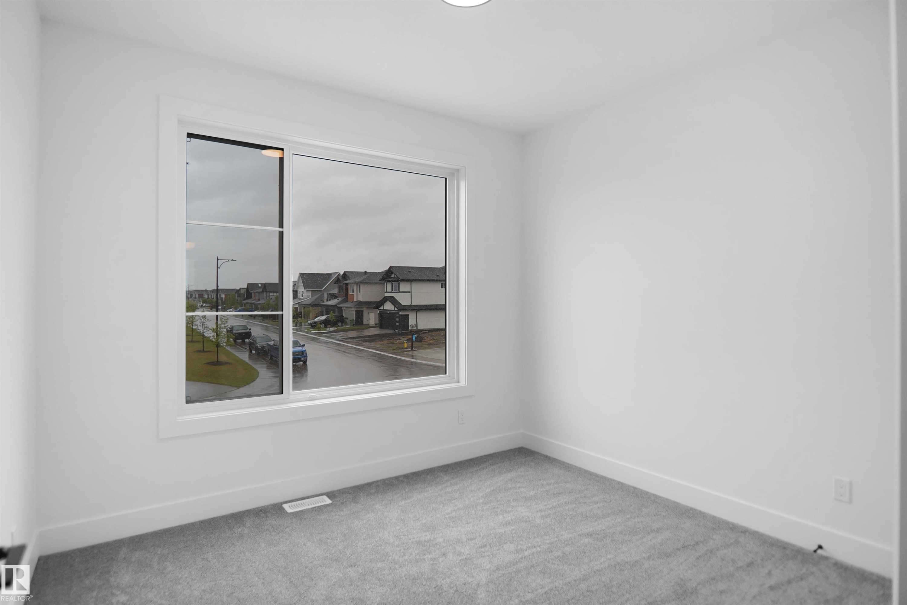 Bright room featuring a large window, neutral gray carpeting, white baseboards, and white painted walls - 142 Edgewater Circle, Leduc, AB