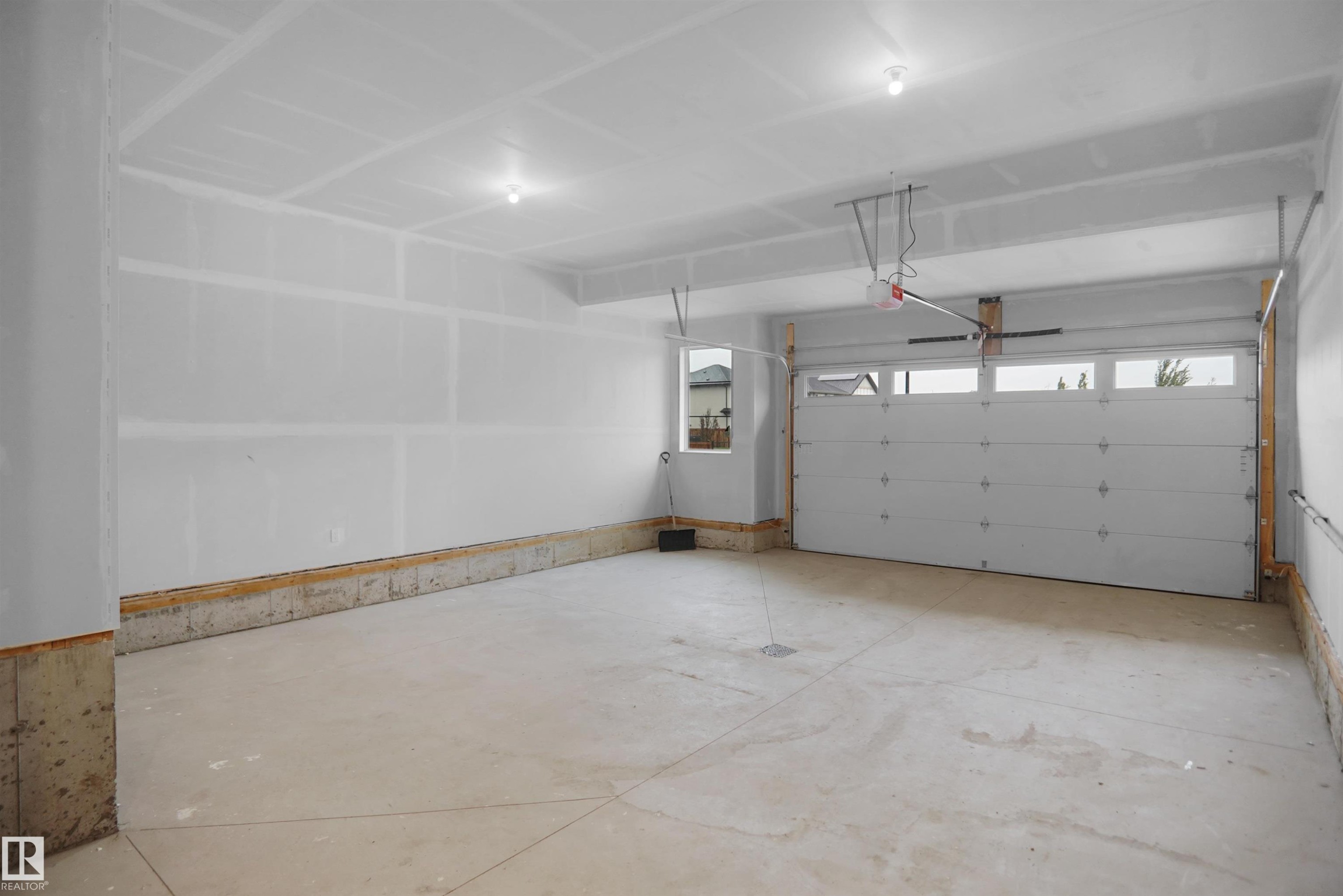 Spacious garage featuring a concrete floor, overhead lighting, and a window for natural light - 142 Edgewater Circle, Leduc, AB