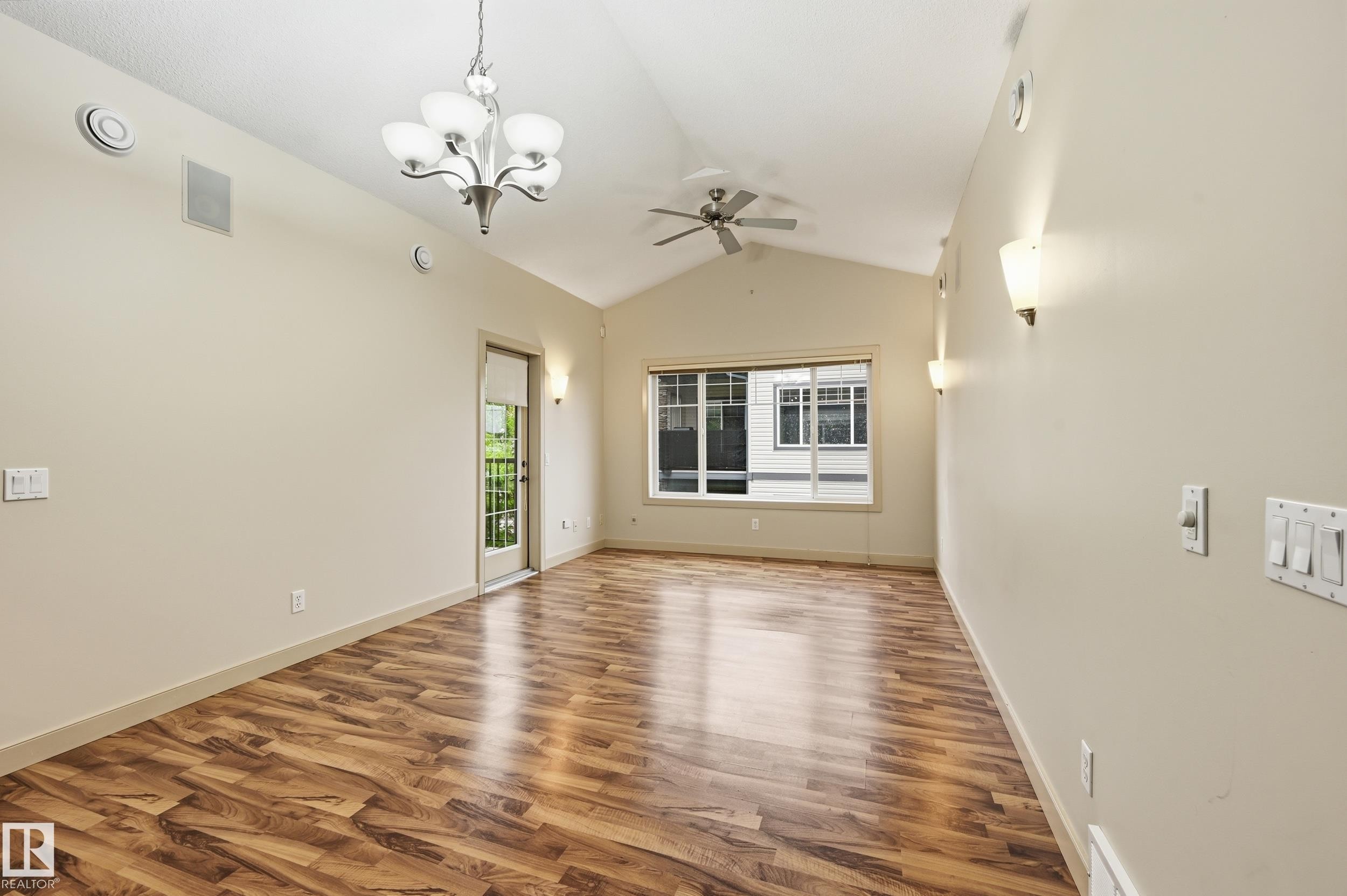 Open-concept room featuring vaulted ceilings, wood-finish flooring, a ceiling fan, a chandelier, and multiple wall sconces - 50 2565 Hanna Crescent, Edmonton, AB