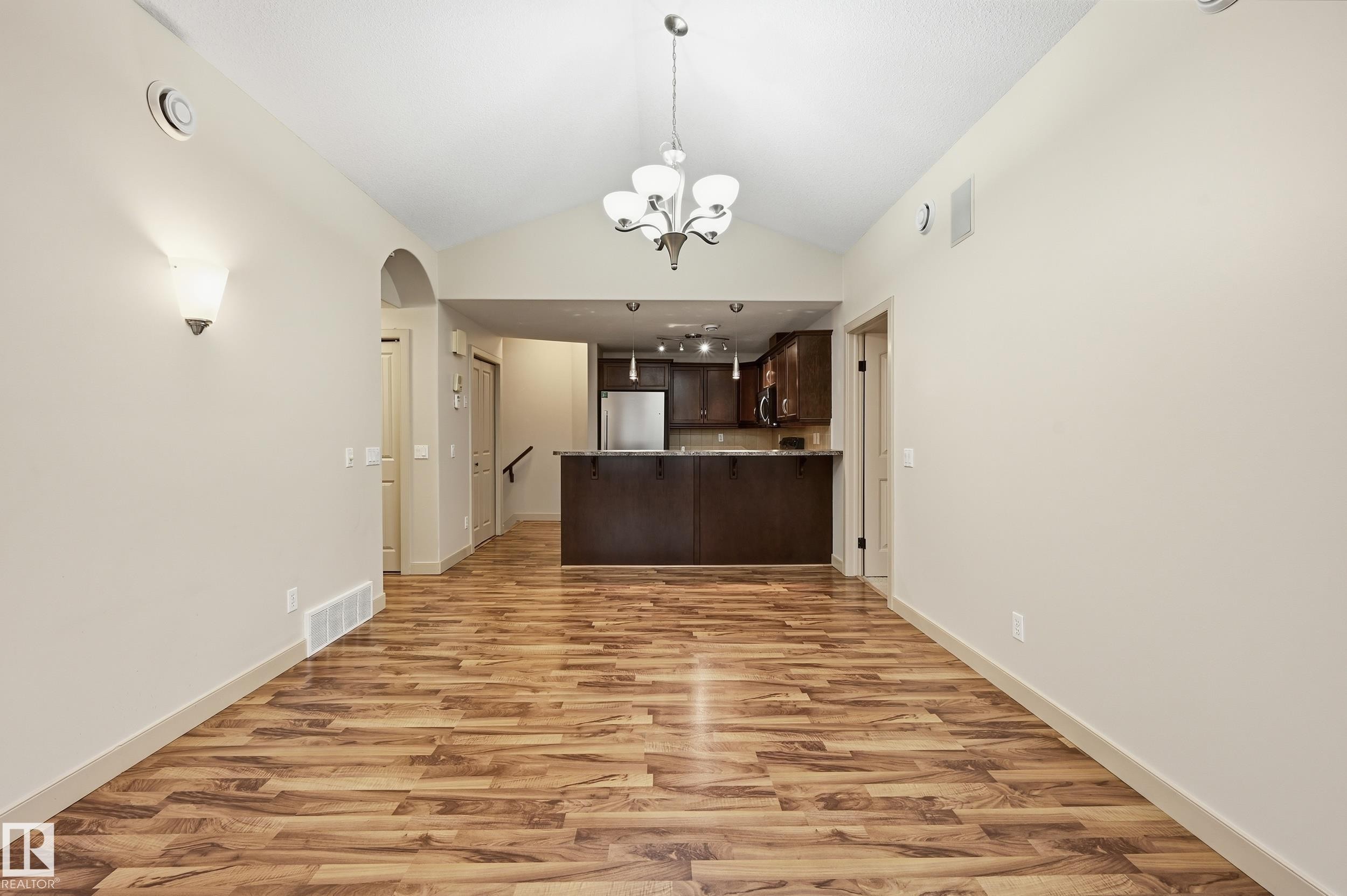 Vaulted ceiling dining area featuring wood-finish flooring, a contemporary chandelier, and two wall sconces - 50 2565 Hanna Crescent, Edmonton, AB