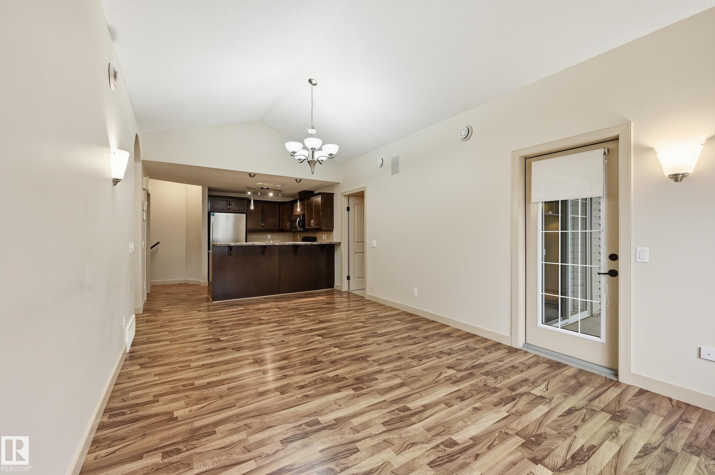 Open-concept living space featuring wood-finish flooring, vaulted ceilings, and a glass-paneled door - 50 2565 Hanna Crescent, Edmonton, AB