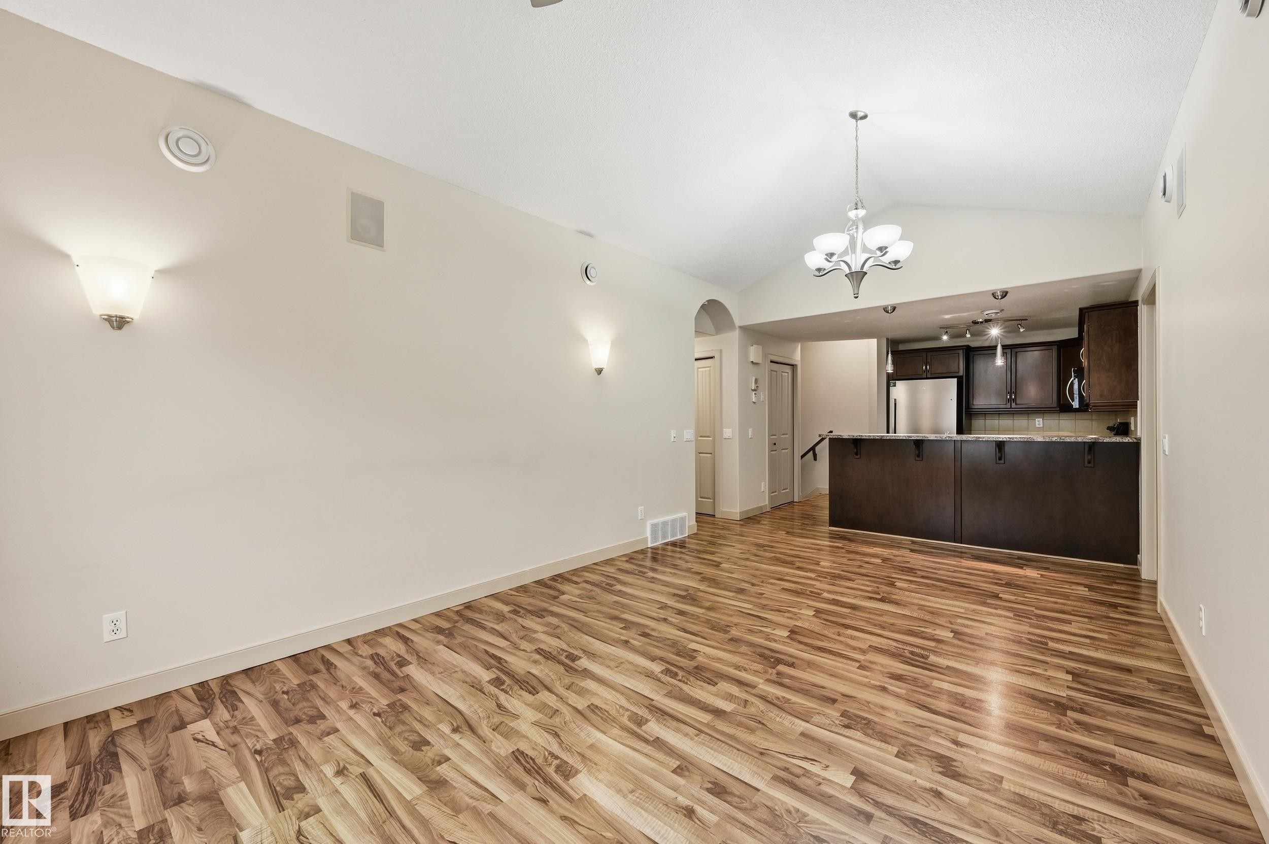 Open-concept living space featuring wood-finish flooring, vaulted ceilings, and an elegant chandelier - 50 2565 Hanna Crescent, Edmonton, AB
