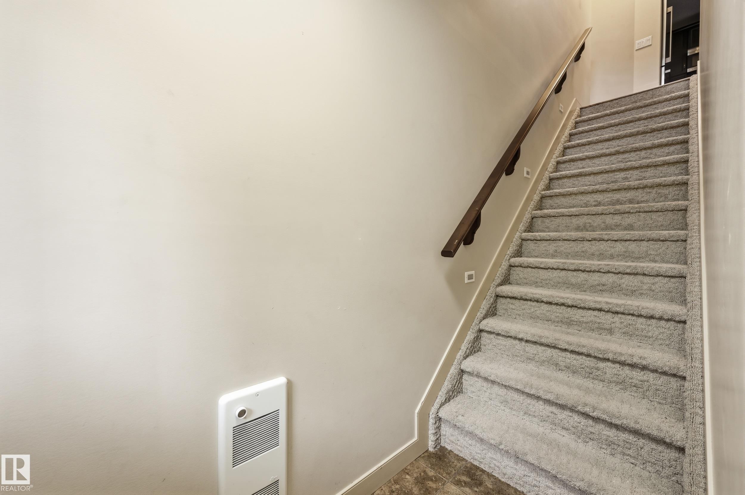 Carpeted staircase featuring a dark wood handrail, recessed wall lighting, and neutral wall paint - 50 2565 Hanna Crescent, Edmonton, AB
