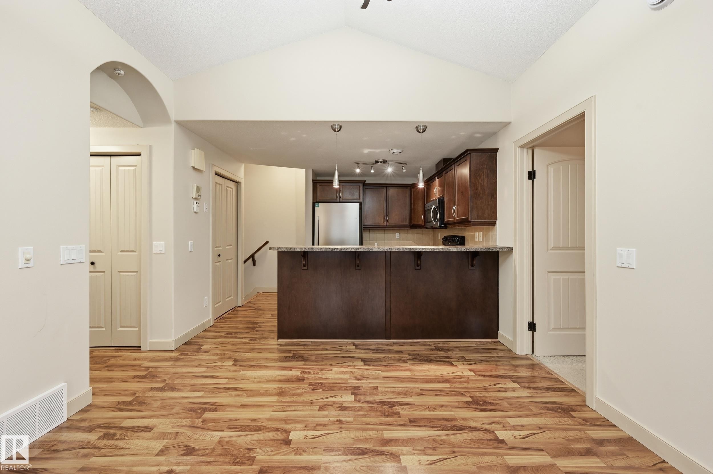 Spacious room featuring vaulted ceilings, wood-finish flooring, an arched entryway, and a breakfast bar with stone-look countertop - 50 2565 Hanna Crescent, Edmonton, AB