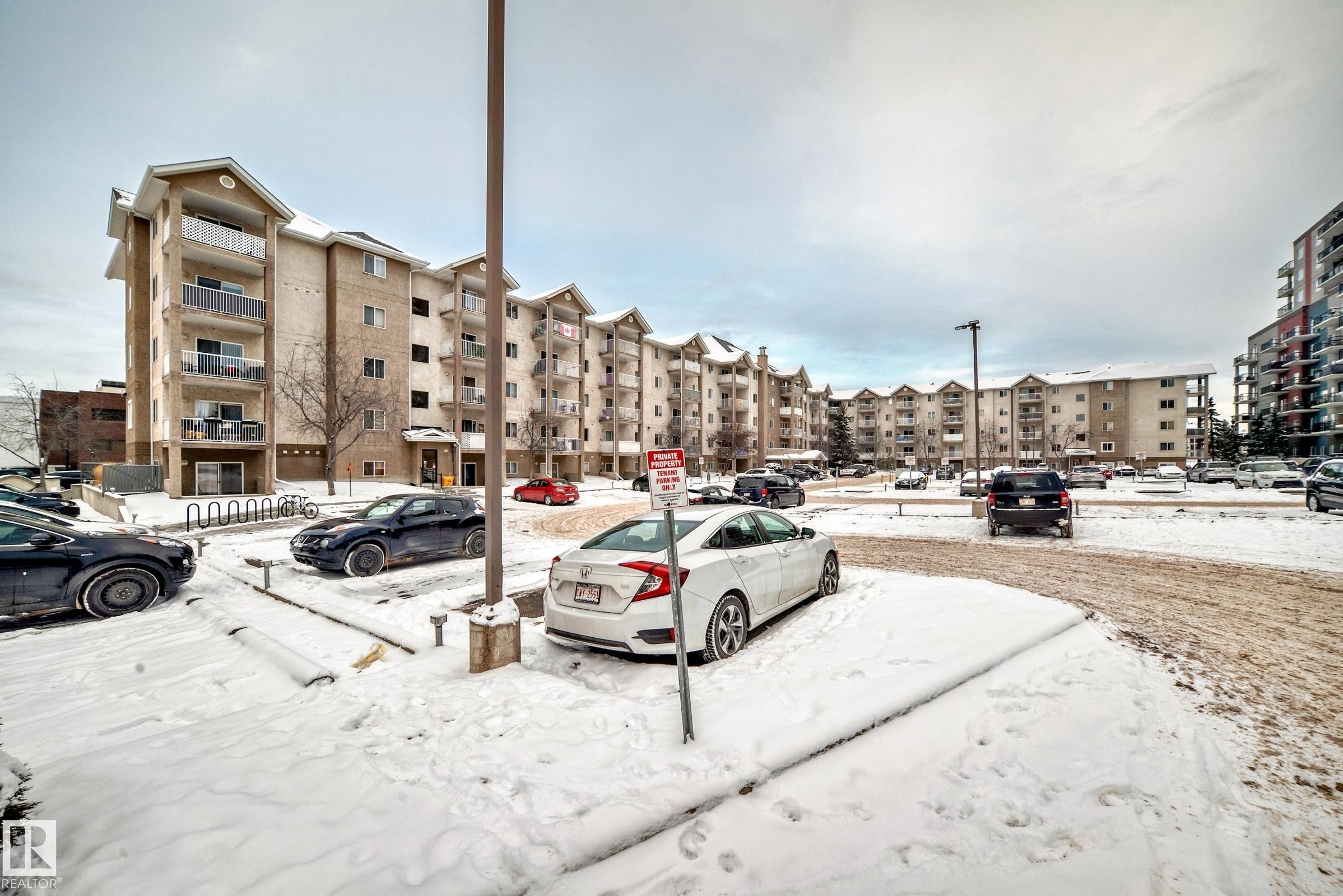 Multi-story residential building featuring light-colored brick and stucco facade, individual balconies with metal railings, and a ground-level entrance - 108 10535 122 Street, Edmonton, AB