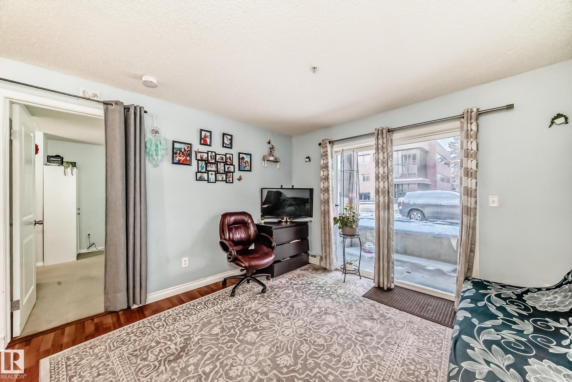 Living area featuring wood-finish flooring, light blue wall paint, and a sliding glass door leading to an outdoor patio - 108 10535 122 Street, Edmonton, AB