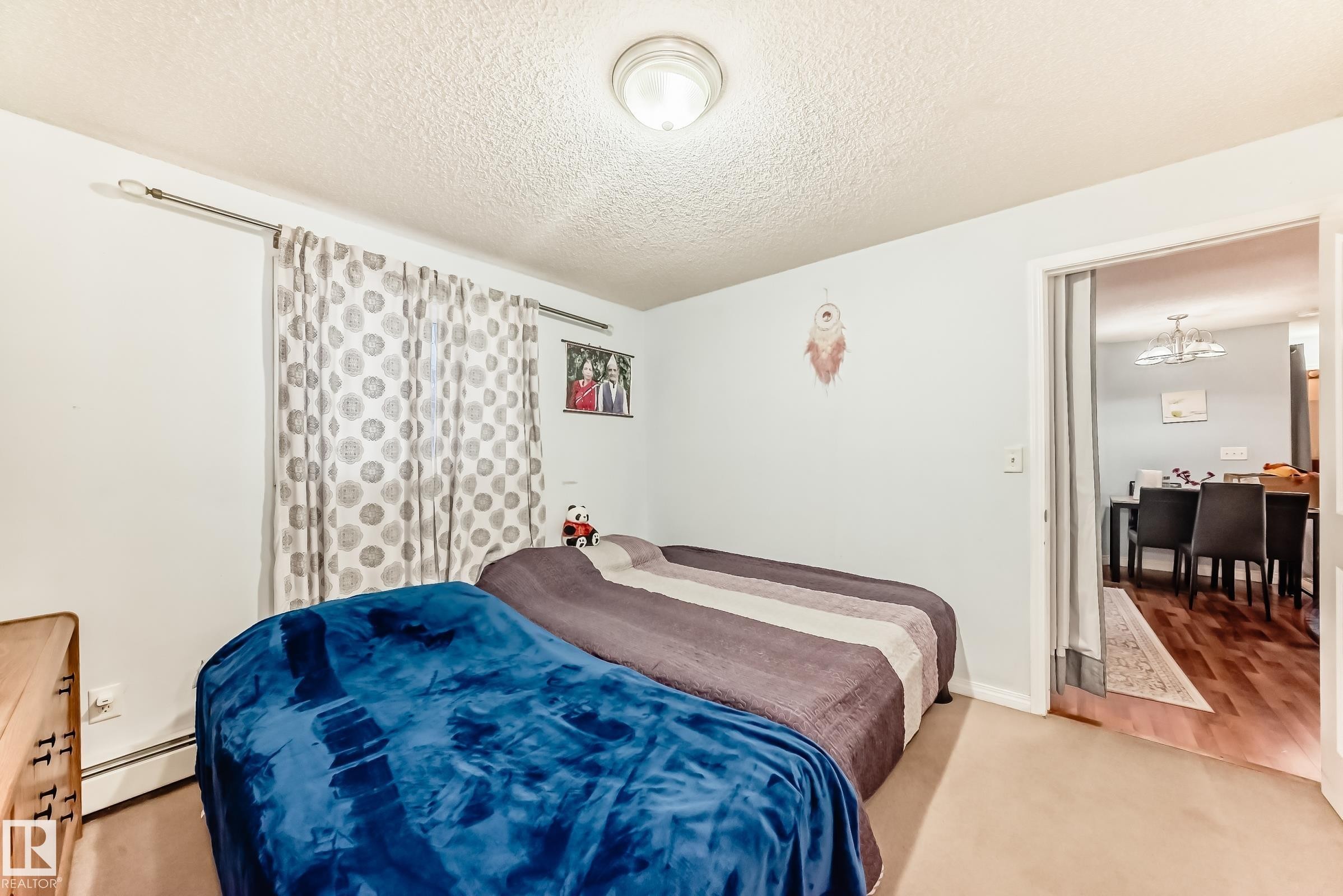 Carpeted room featuring a ceiling-mounted light fixture, light-colored walls, and a window with patterned drapes - 108 10535 122 Street, Edmonton, AB