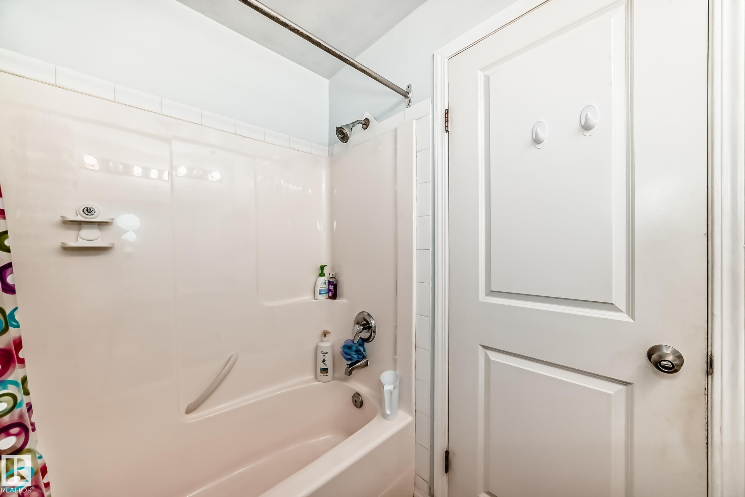 Bathroom featuring a tub/shower combination with a built-in ledge, white tile surround, and a brushed nickel shower head - 108 10535 122 Street, Edmonton, AB