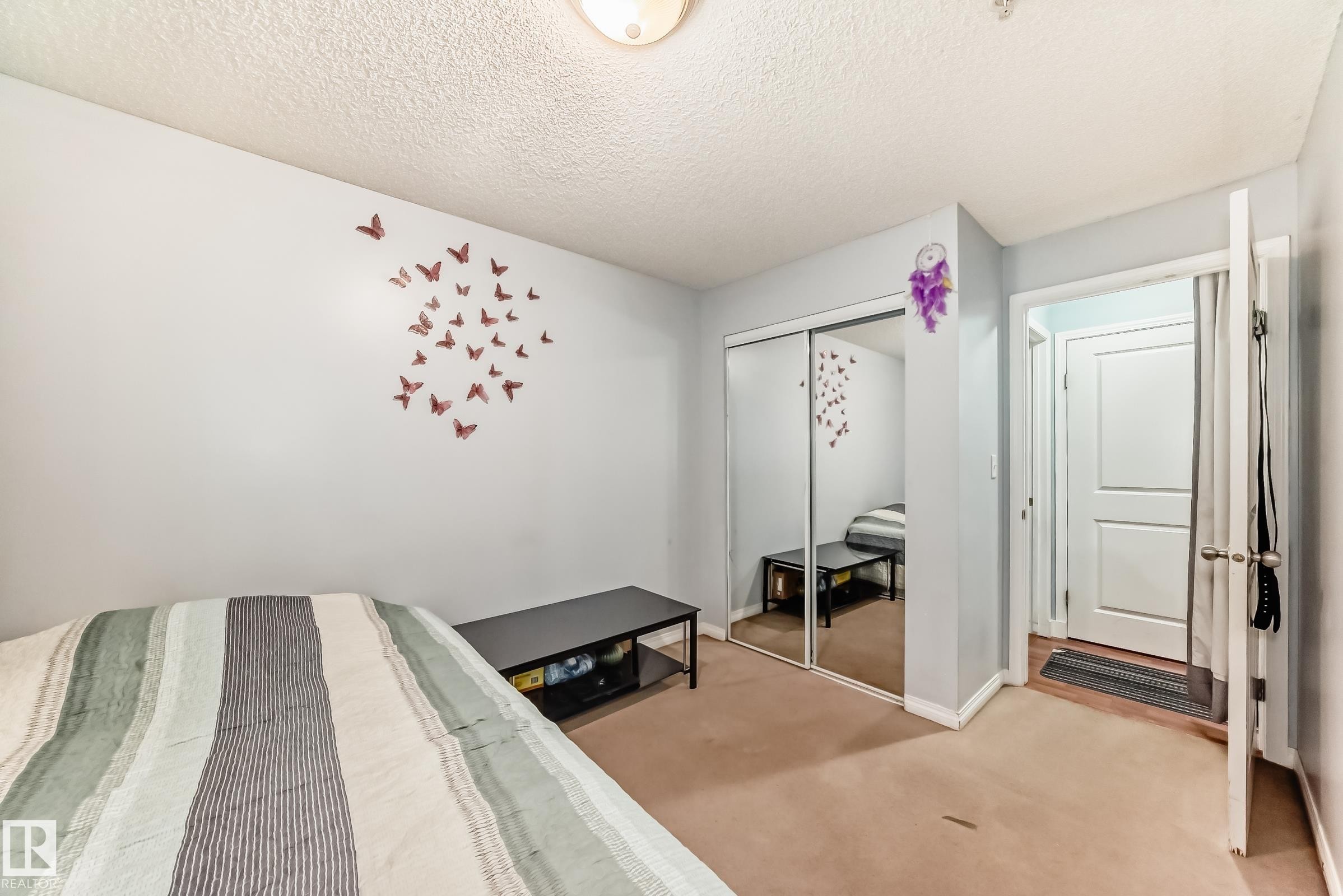 Bedroom featuring wall-to-wall carpeting, mirrored closet doors, and light-colored walls - 108 10535 122 Street, Edmonton, AB