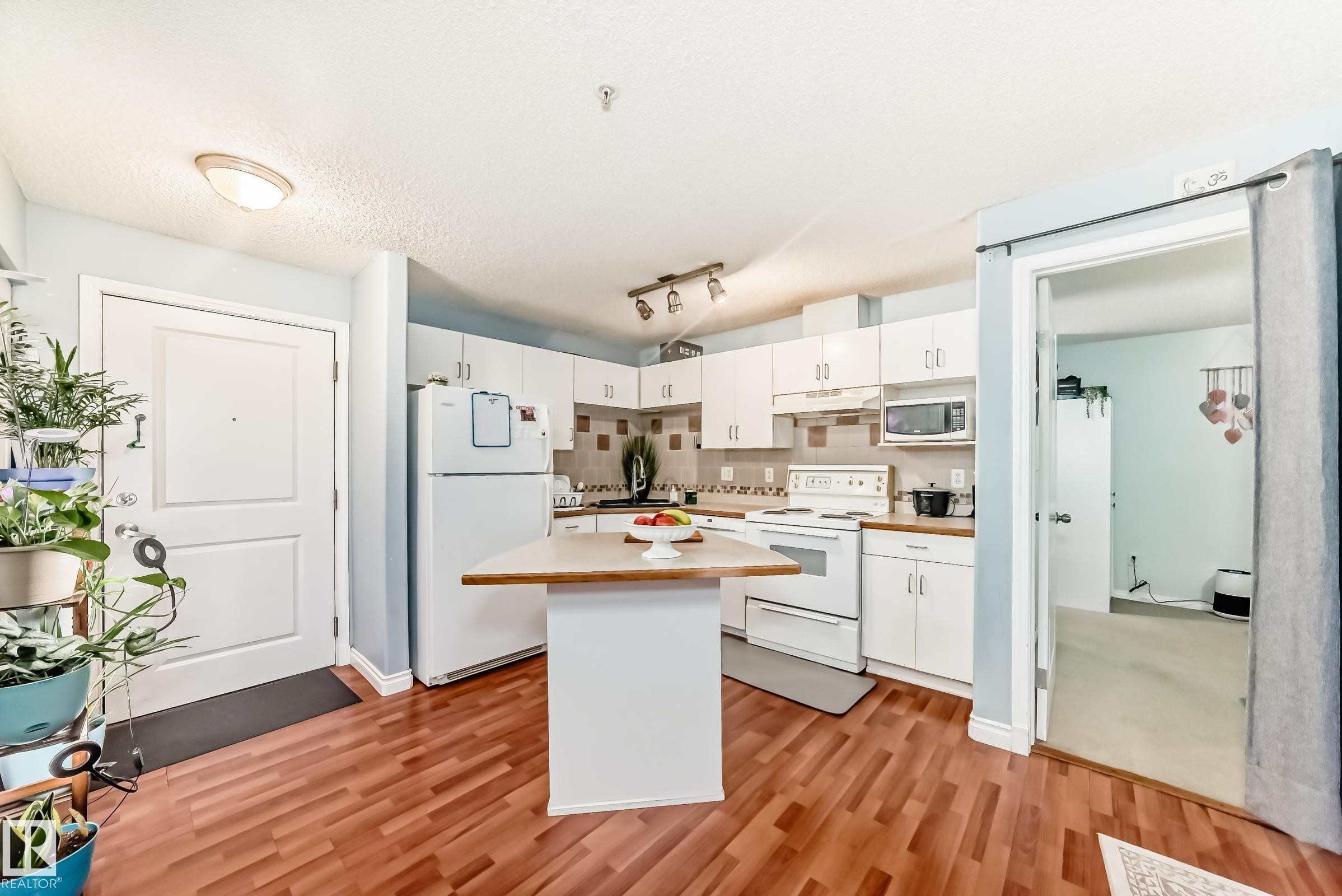 Kitchen featuring white cabinetry, white appliances, a light wood-finish countertop, a central island, and wood-finish flooring - 108 10535 122 Street, Edmonton, AB