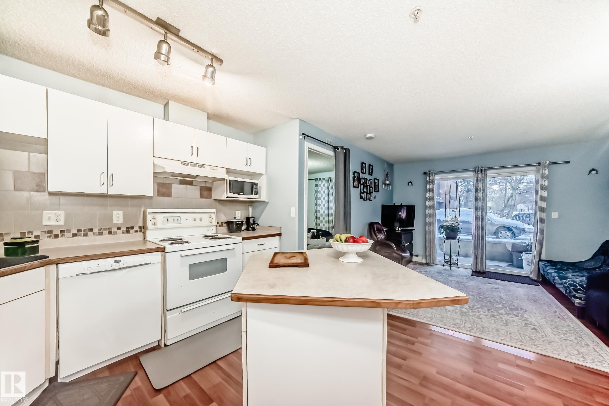 Open-concept living area featuring wood-finish flooring, white cabinetry, a tile backsplash, and a breakfast bar - 108 10535 122 Street, Edmonton, AB