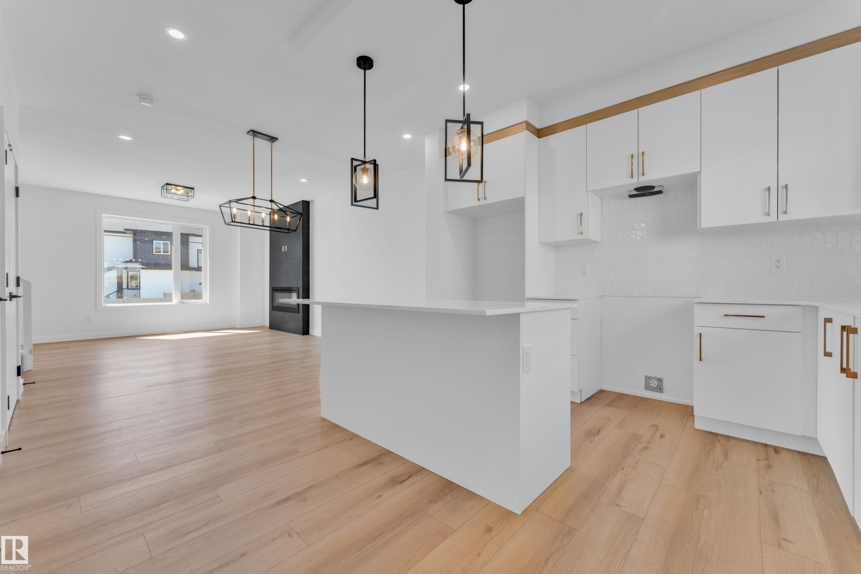 Modern kitchen featuring white cabinetry with gold-tone hardware, white subway tile backsplash, a white island, and wood-finish flooring - 177 Graybriar Drive, Stony Plain, AB