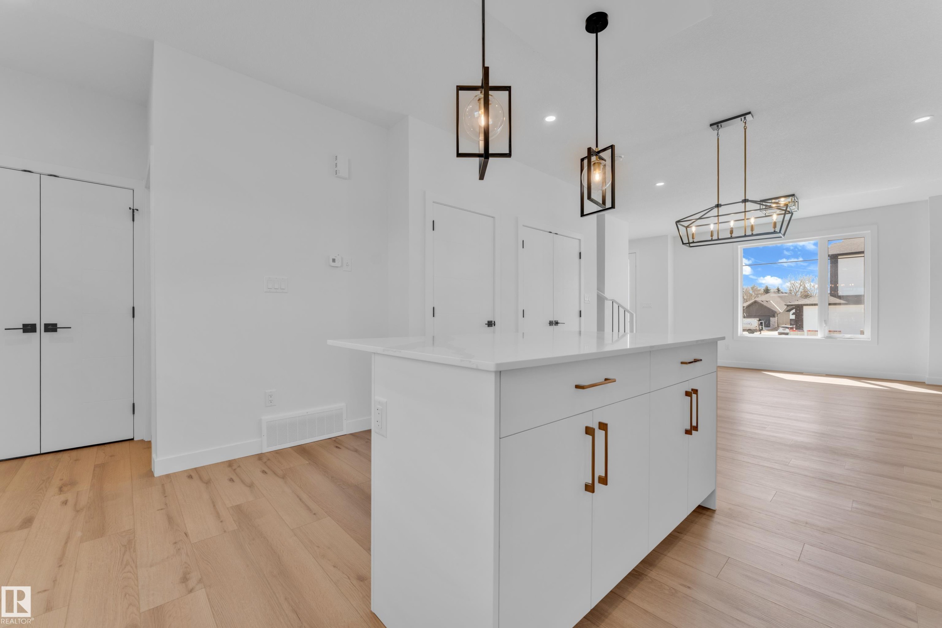 Kitchen island with a white countertop and bronze hardware, wood-finish flooring, two modern pendant lights, and a linear chandelier - 177 Graybriar Drive, Stony Plain, AB