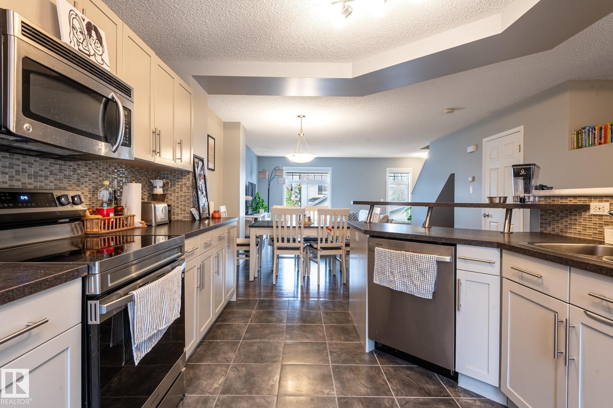 Kitchen featuring stainless steel appliances, light-toned cabinetry, dark countertops, and a mosaic tile backsplash - 46 465 Hemingway Road, Edmonton, AB
