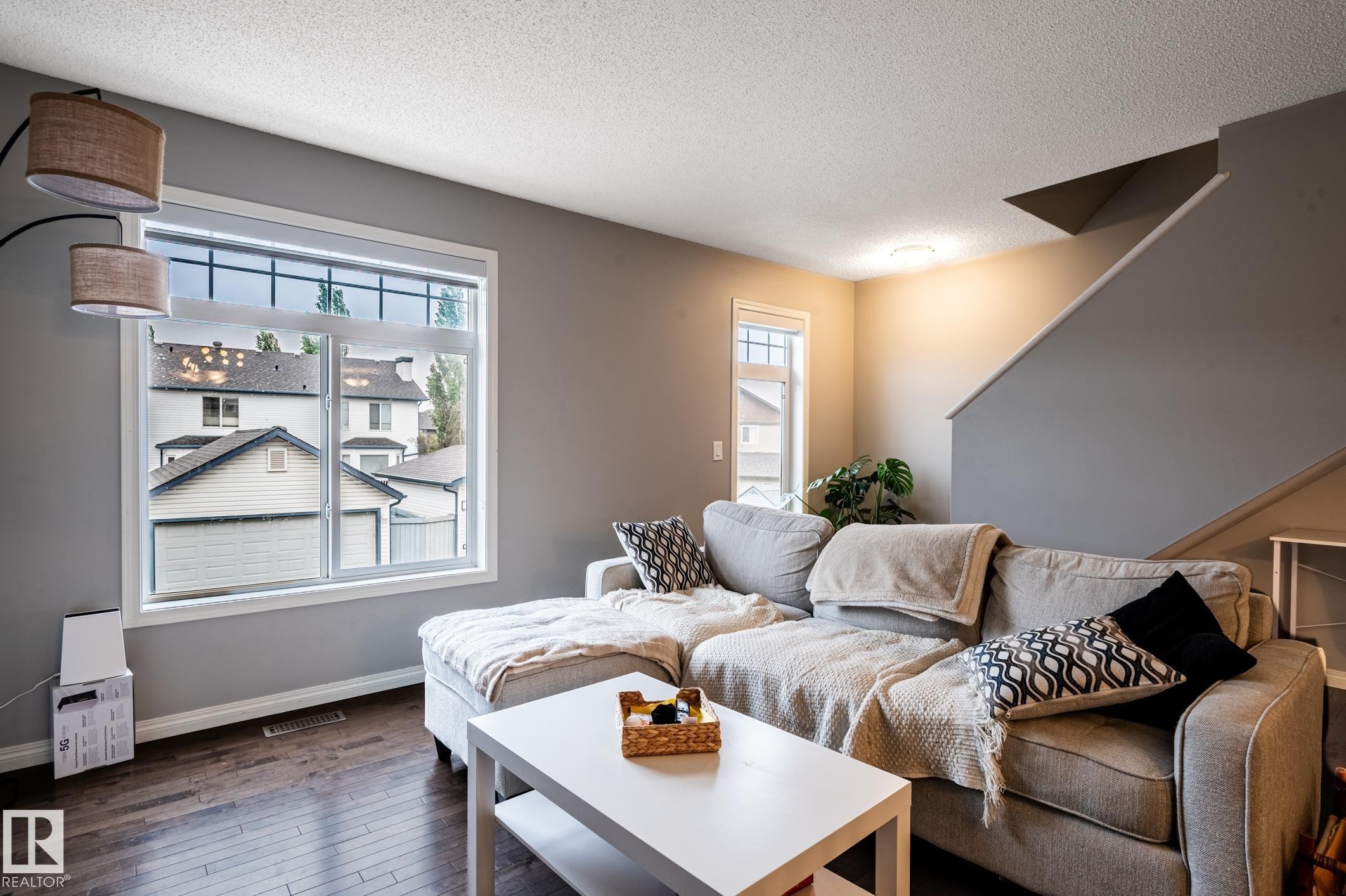Living area featuring wood-finish flooring, a large multi-pane window with white trim, and a contemporary ceiling fixture - 46 465 Hemingway Road, Edmonton, AB