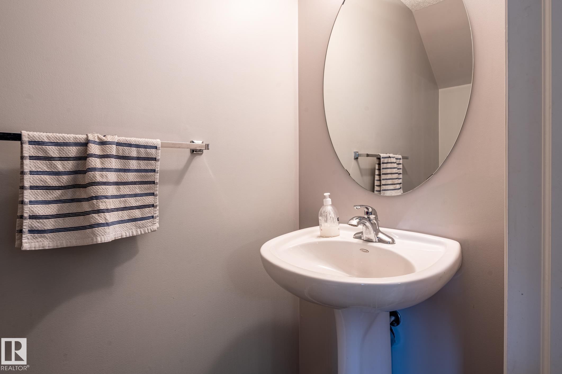 Pedestal sink with chrome faucet, complemented by an oval wall-mounted mirror - 46 465 Hemingway Road, Edmonton, AB