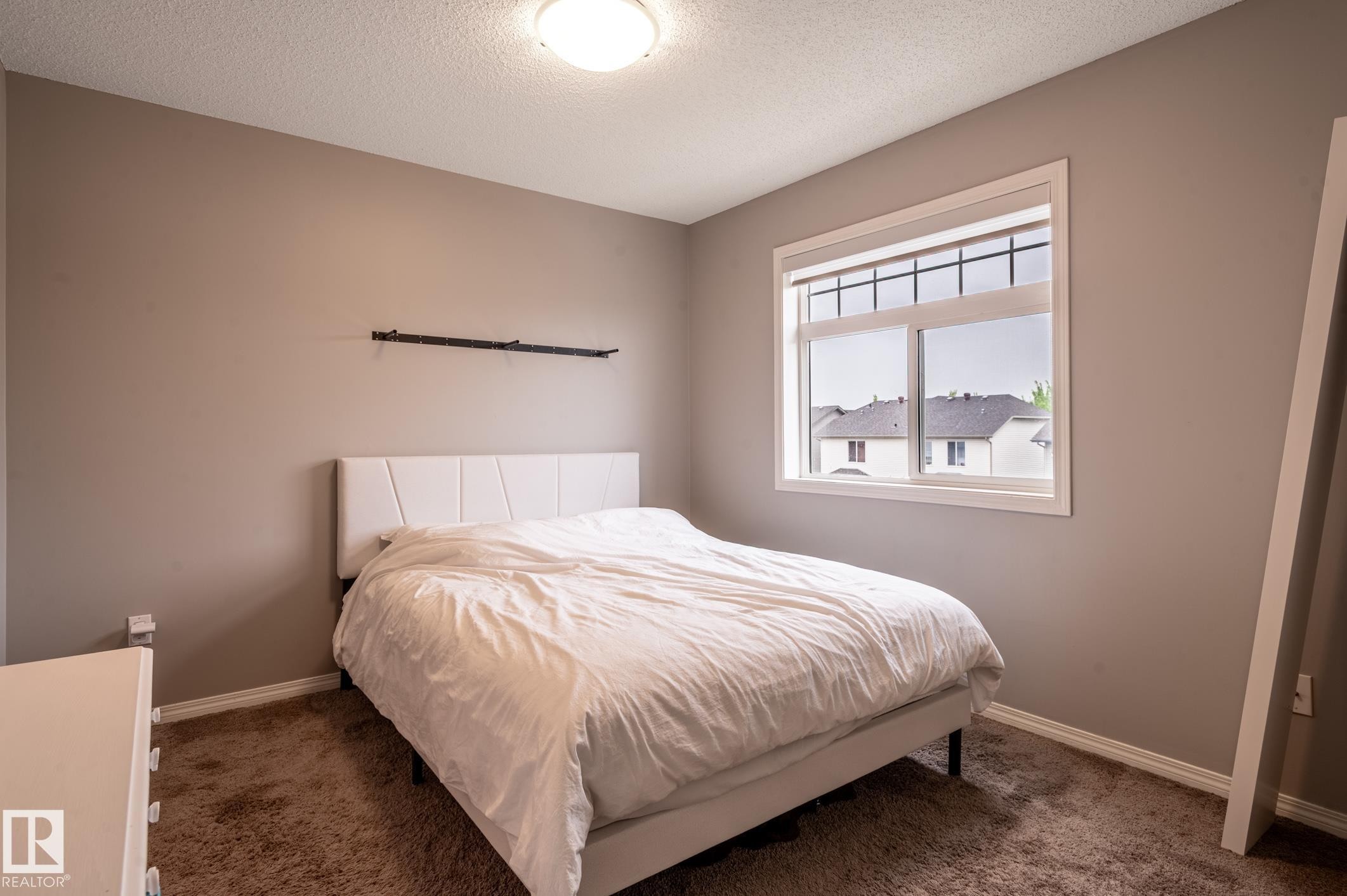 Bedroom featuring neutral-toned walls, brown carpet flooring, and a large window with white trim - 46 465 Hemingway Road, Edmonton, AB