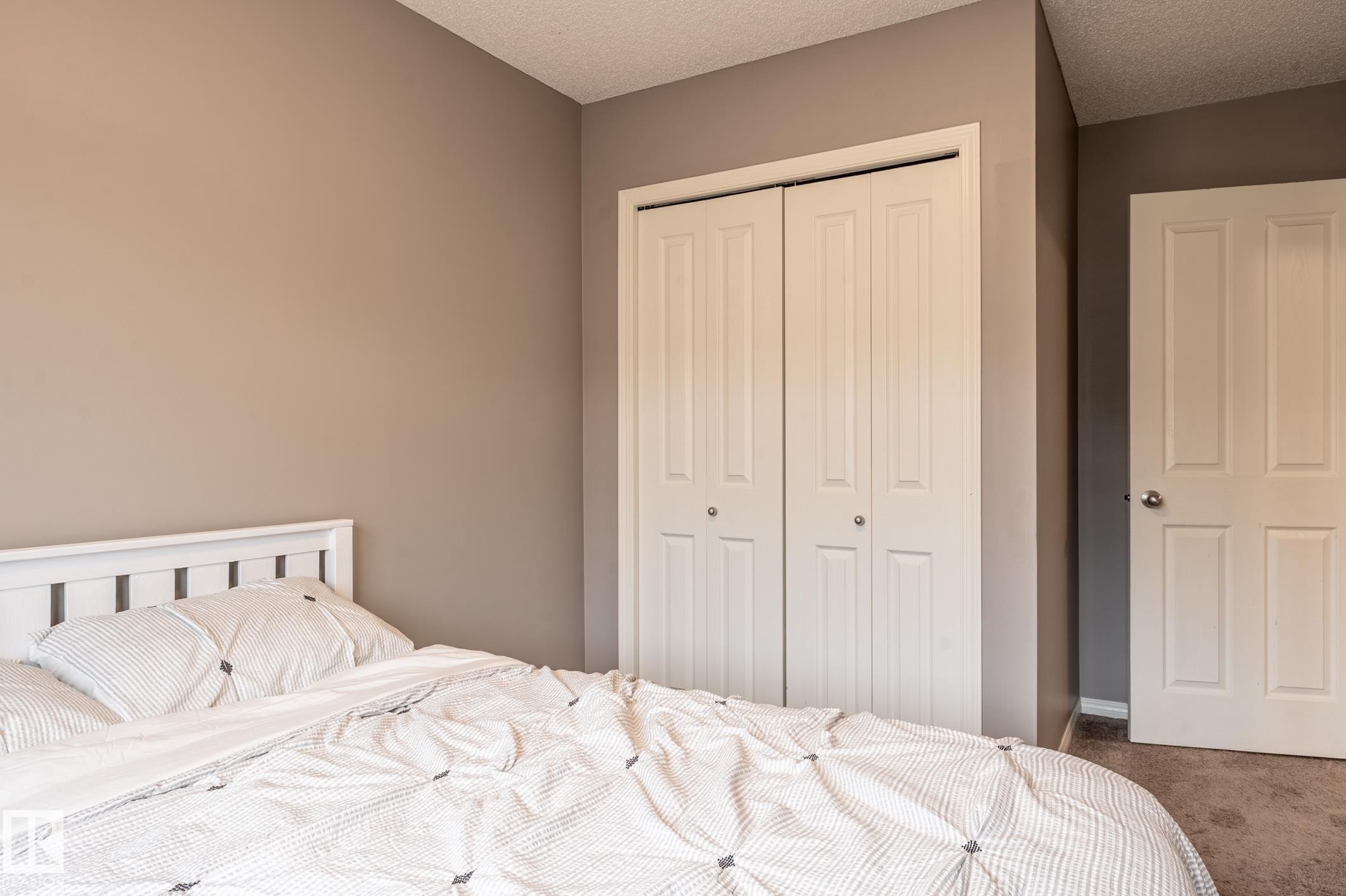 Room featuring a white paneled bi-fold closet, a white paneled door, neutral-toned walls, textured ceiling, and carpeted flooring - 46 465 Hemingway Road, Edmonton, AB