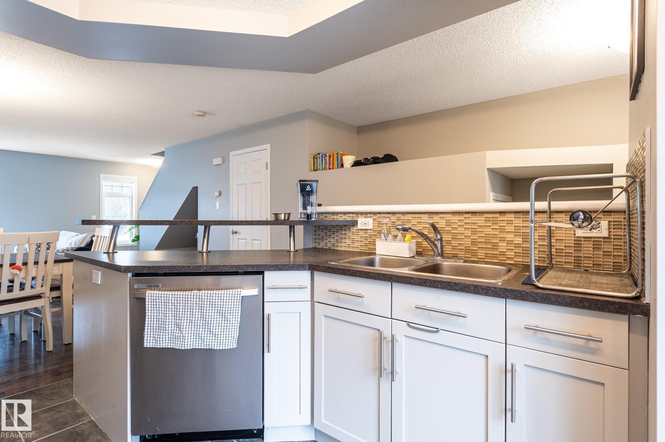 Kitchen featuring a stainless steel dishwasher, double basin sink, and mosaic tile backsplash - 46 465 Hemingway Road, Edmonton, AB