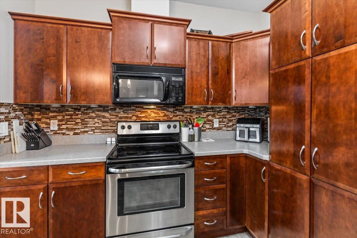 Kitchen featuring wood cabinetry, stainless steel range, built-in microwave, and a mosaic tile backsplash - 229 41 Summerwood Boulevard, Sherwood Park, AB - Indoor Photo Showing Kitchen