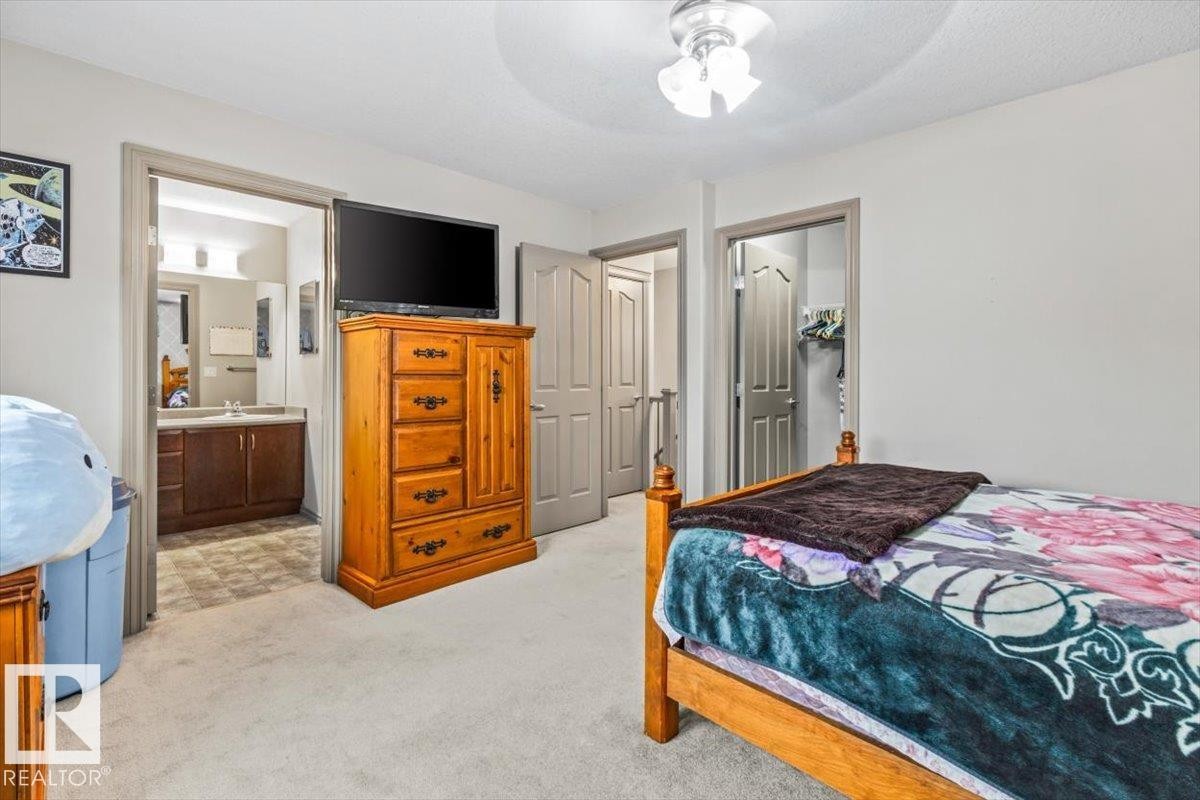 Carpeted bedroom featuring a light gray wall color, a flush mount ceiling light, and an open doorway revealing a bathroom with a dark wood vanity - 229 41 Summerwood Boulevard, Sherwood Park, AB - Indoor Photo Showing Bedroom