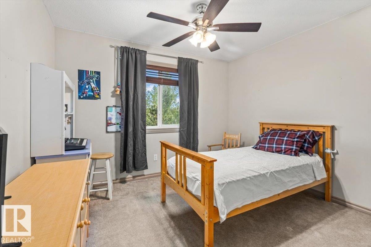 Carpeted room featuring a ceiling fan with integrated lighting, a window with horizontal blinds, and a built-in wall shelf - 229 41 Summerwood Boulevard, Sherwood Park, AB - Indoor Photo Showing Bedroom